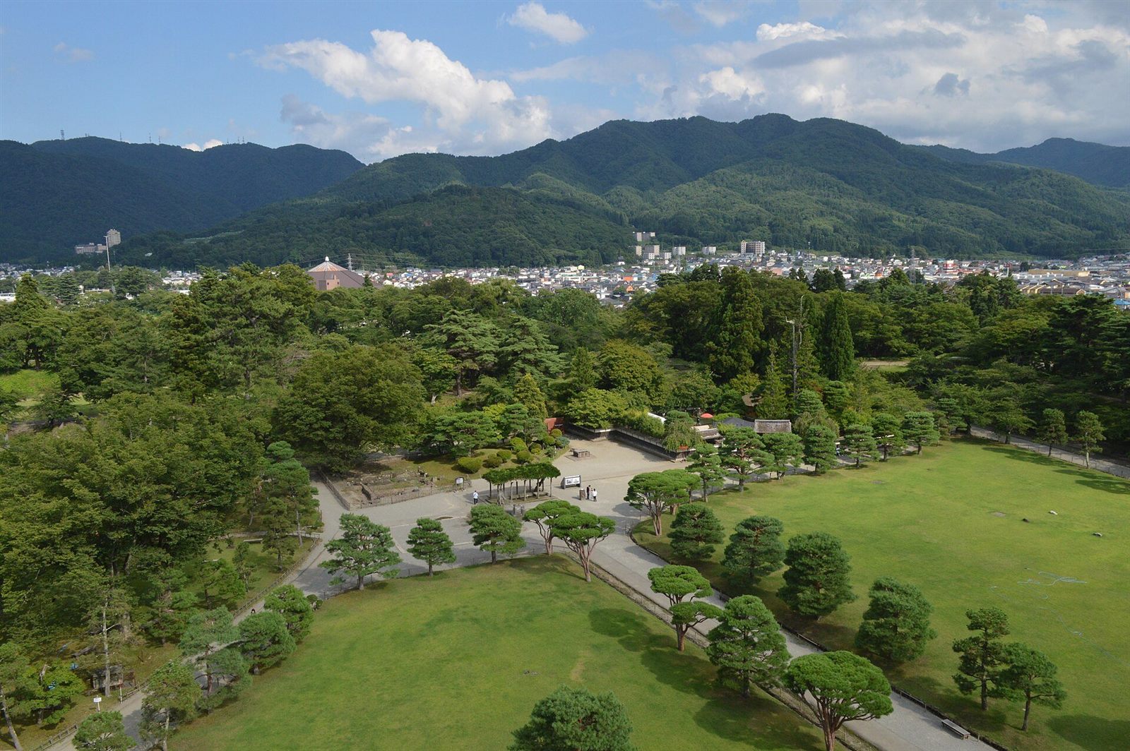 天守閣の上から、城跡の緑の公園と会津若松の町、遠くの山並みを見下ろす