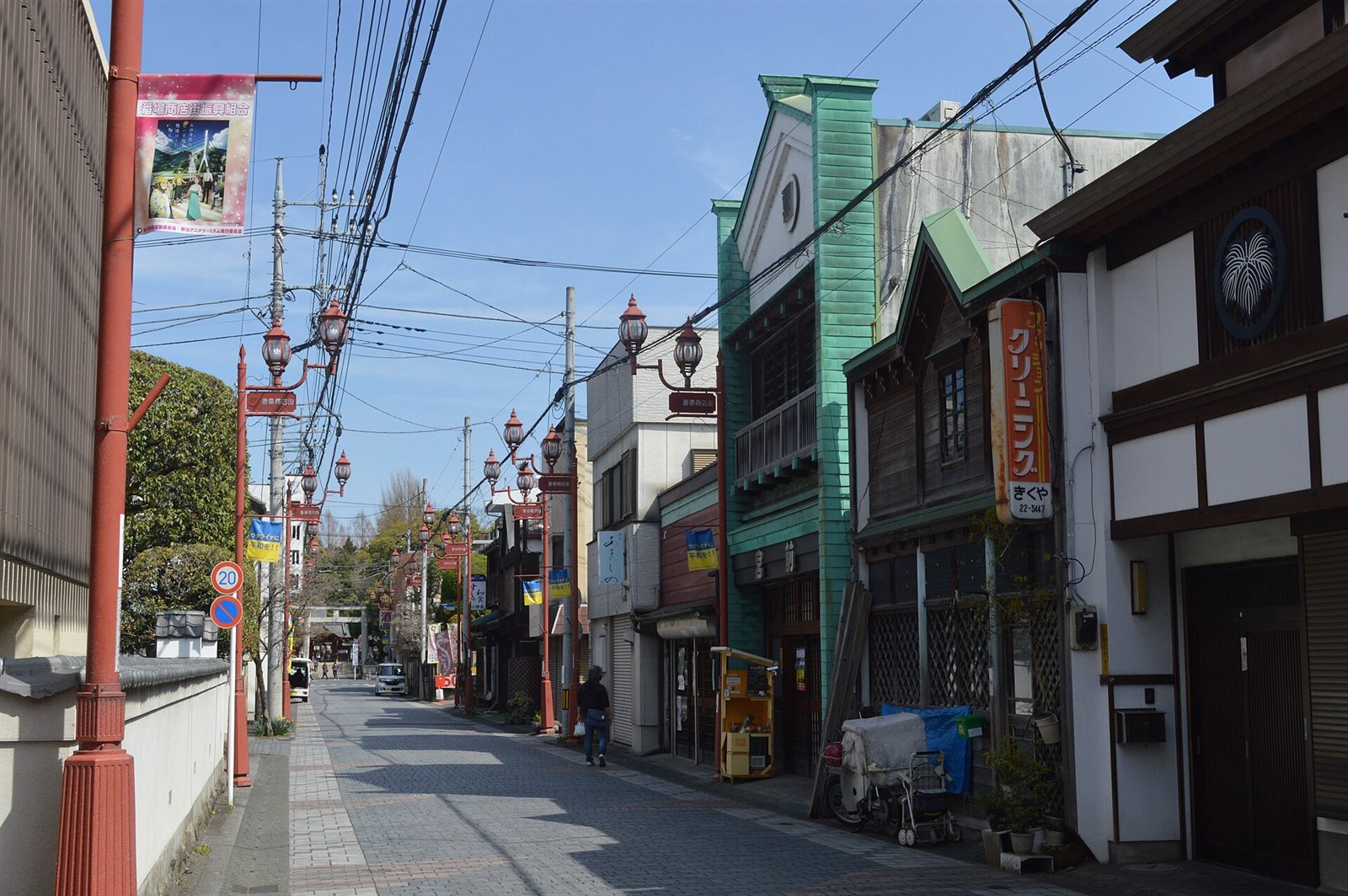 石畳の番場通り。右手に緑色の外壁の古い商店建築が並び、赤い街灯が続く通りの奥に鳥居が見える