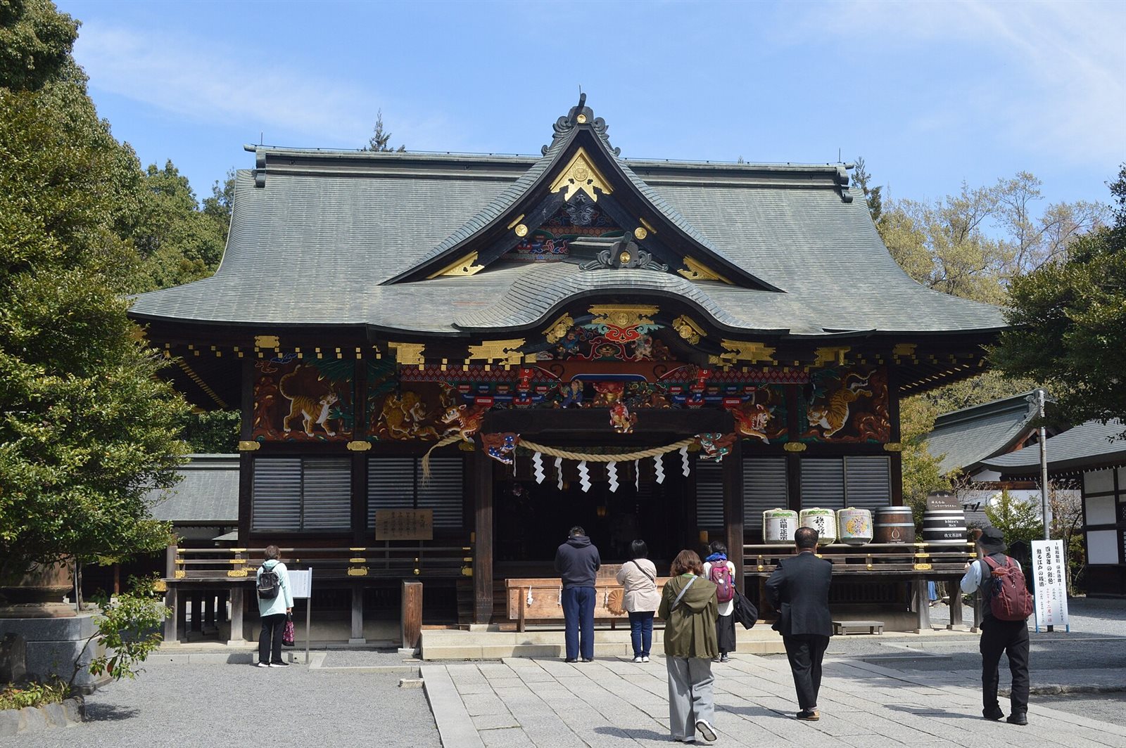 秩父神社の拝殿。緑青色の屋根の下、正面の軒に虎や龍の極彩色の彫刻が並び、石畳の参道で参拝者が拝殿に向かっている