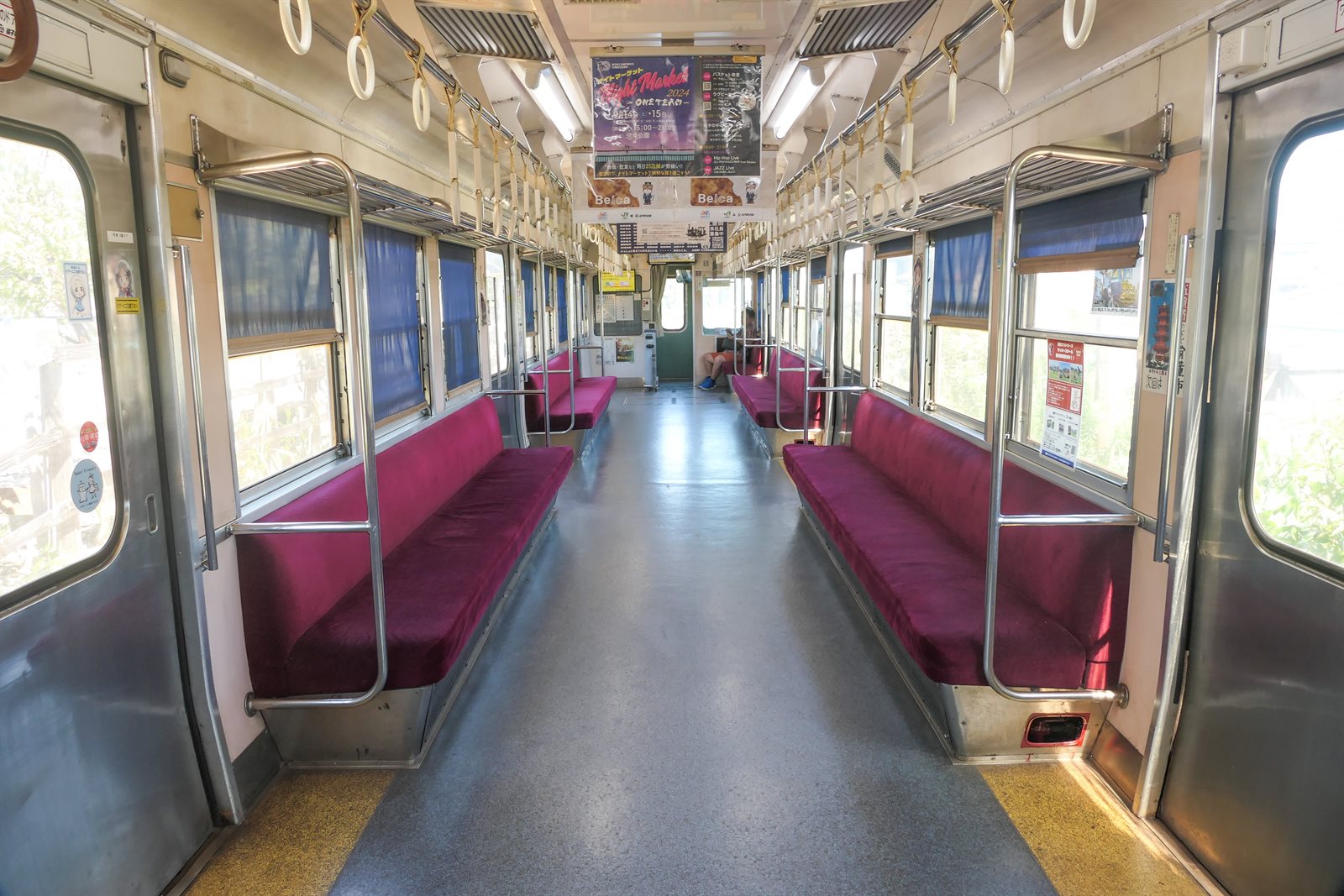 銚子電鉄の車内。通路の両側に赤い布張りのロングシートが続き、天井につり革と網棚、両側の窓に日よけが下りている