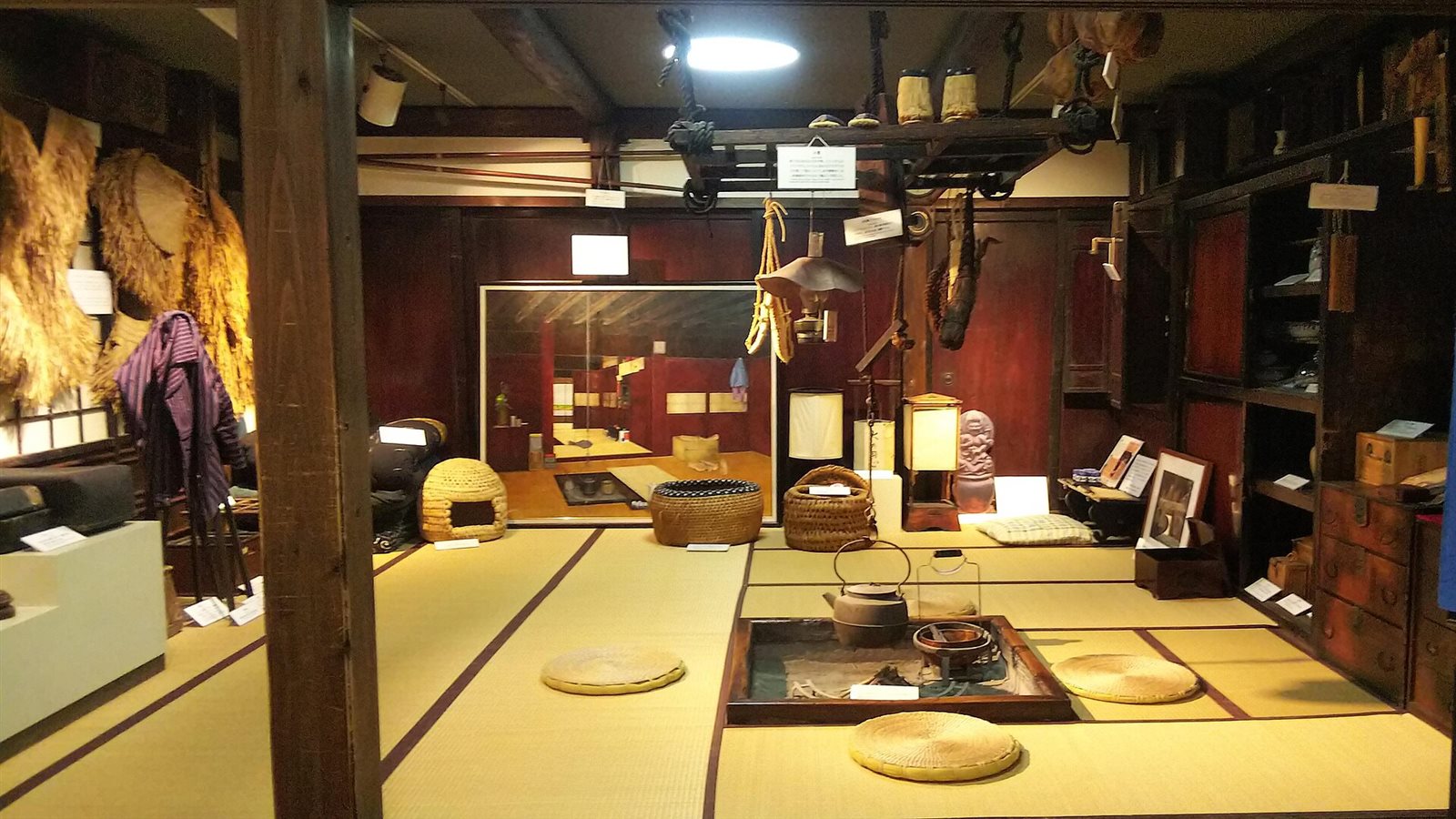 囲炉裏のある畳の部屋に、蓑や籠などの昔の道具が並ぶ雪国館の展示