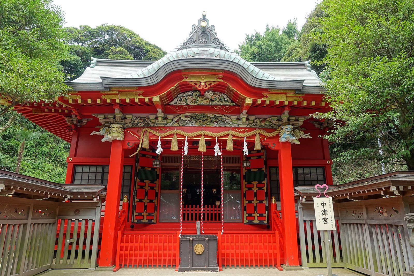 朱色の柱と金色の彫刻が施された江島神社中津宮の社殿の正面。左右を緑の木々が囲む