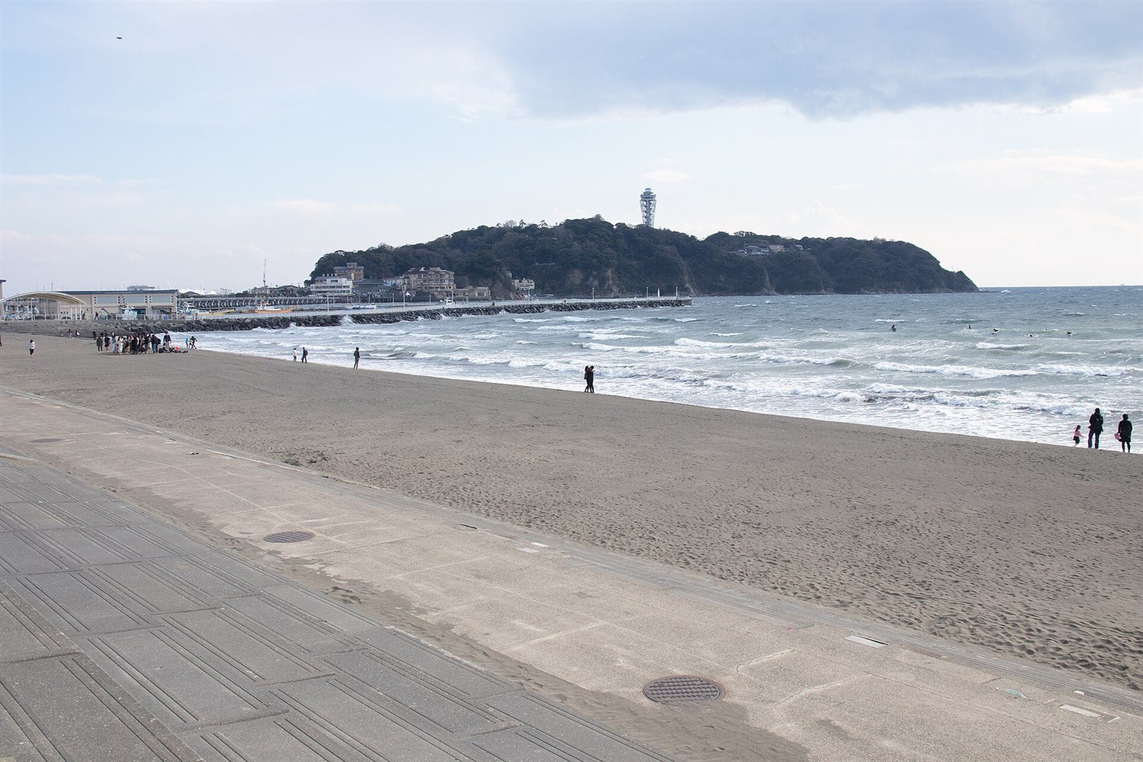 片瀬海岸の砂浜の向こうに、緑の島と展望灯台が見える江の島