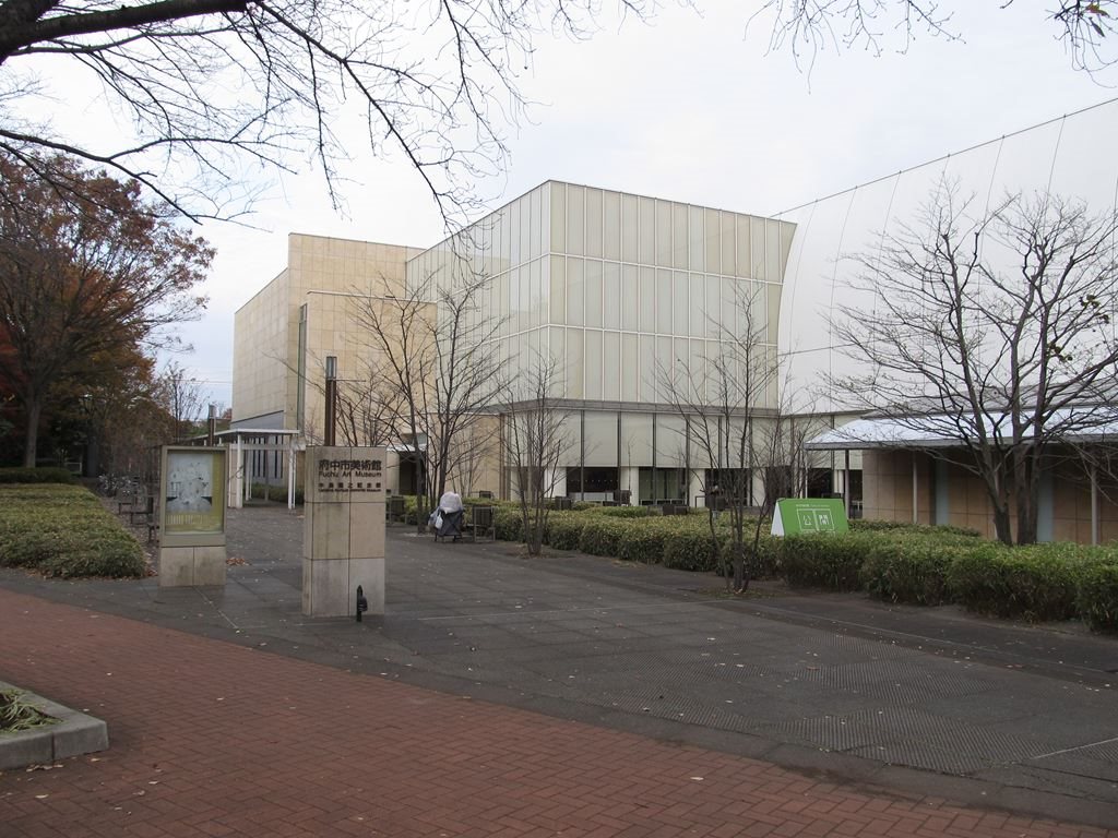 木々に囲まれた、府中市美術館の建物と入口の案内板