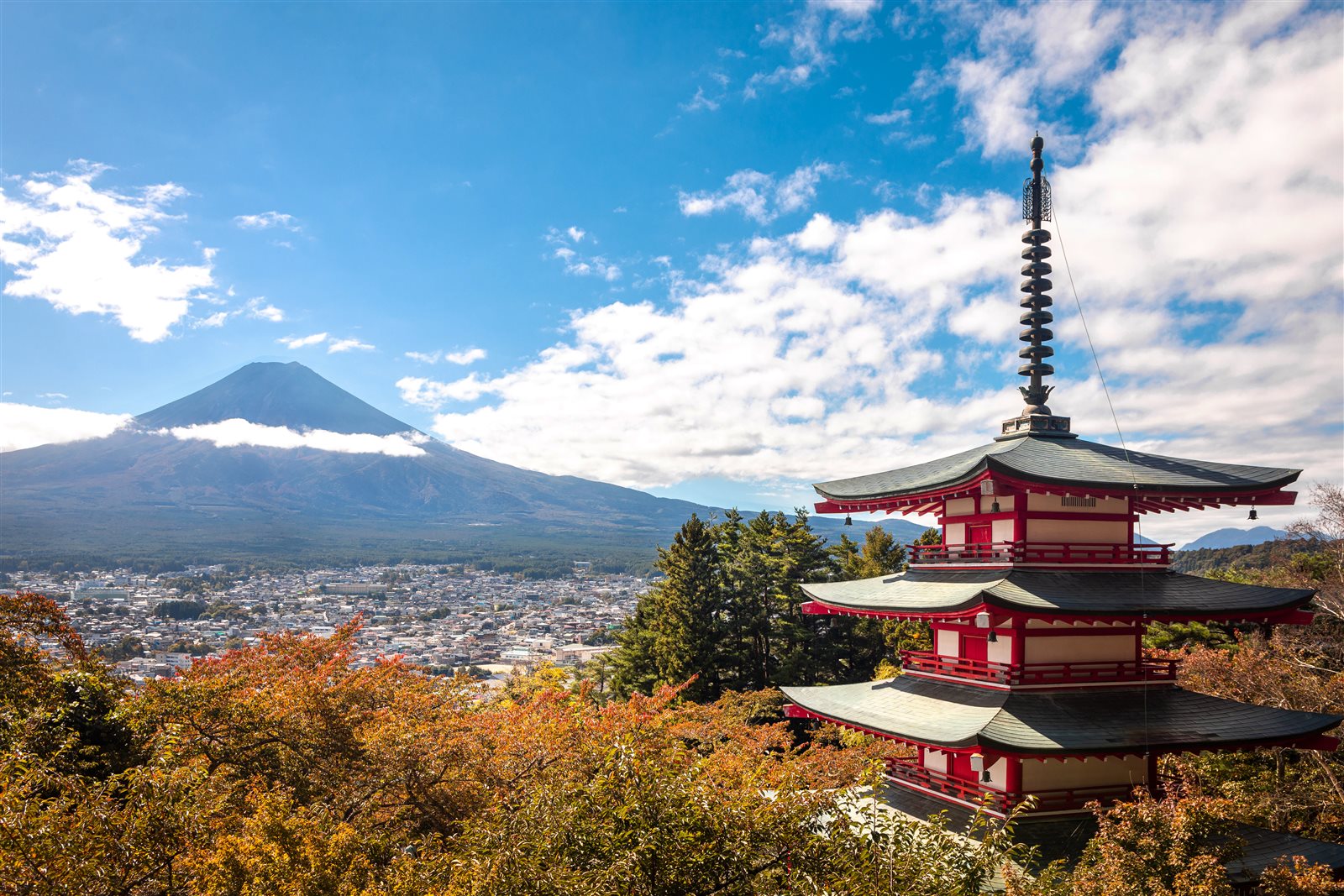 紅葉の木々の向こうに富士山と富士吉田の街並みが広がり、右に朱色の五重塔が立つ