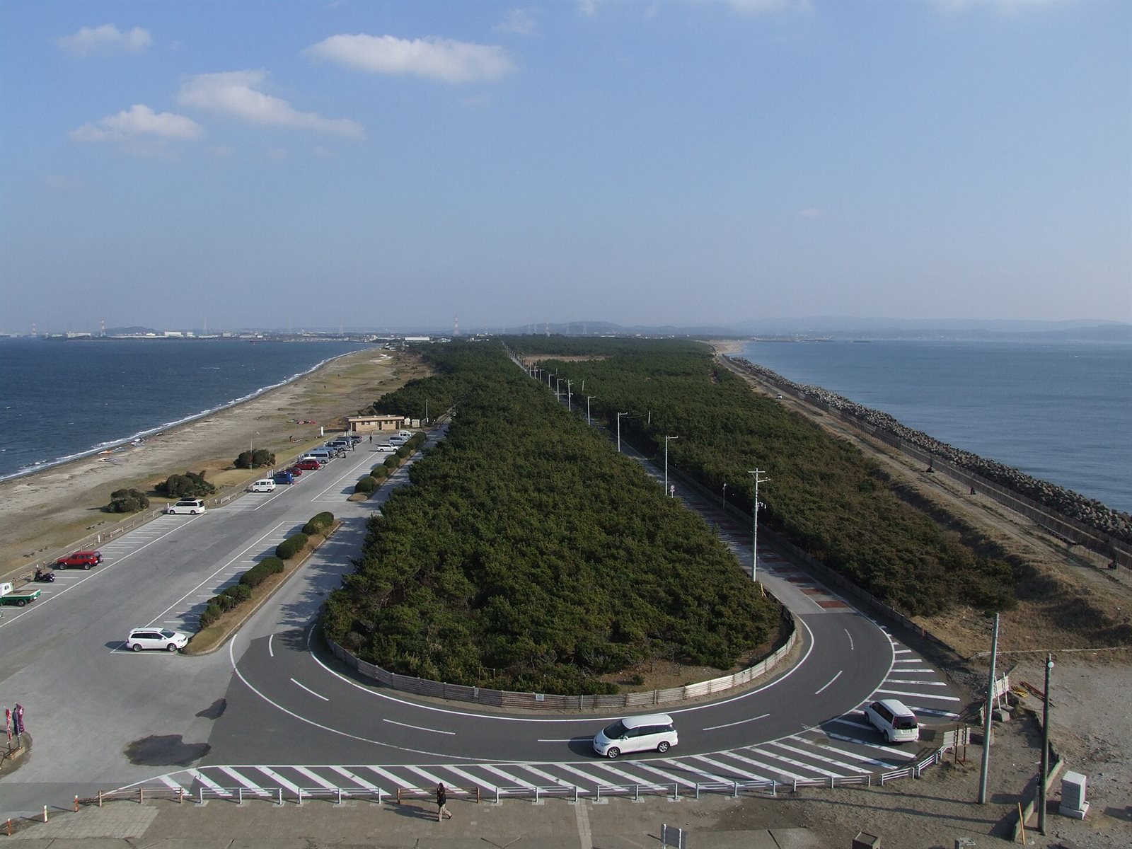 明治百年記念展望塔の上から見た富津岬。左右を海にはさまれた細長い砂洲に松林が続き、手前に駐車場と道路の折り返しがある