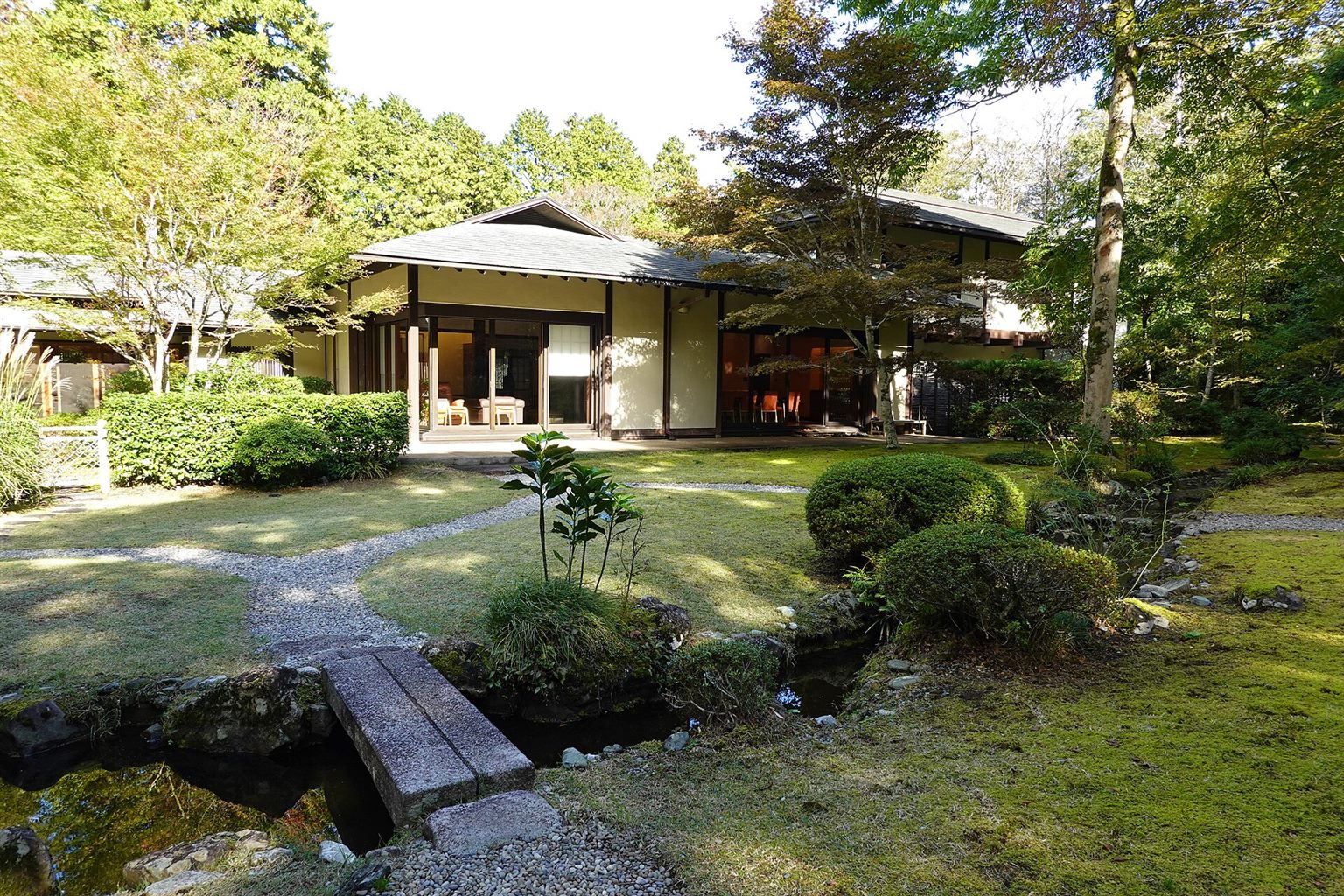 小さな橋のかかる流れと芝生の庭の向こうに建つ、東山旧岸邸の平屋の建物