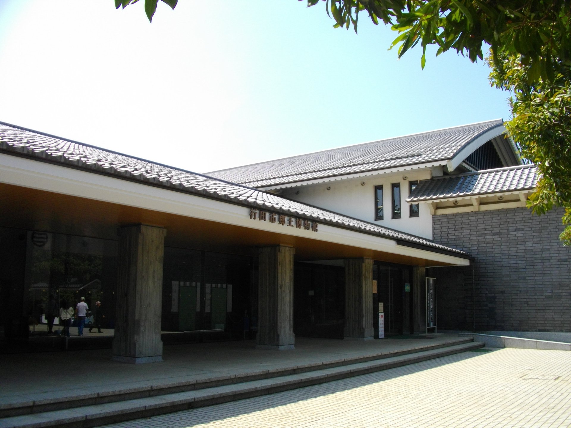 瓦屋根の大きな庇と石の柱が並ぶ、行田市郷土博物館の入口