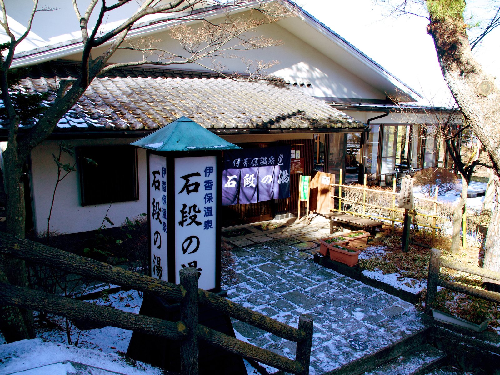 雪の残る伊香保温泉石段の湯の入口。「石段の湯」と書かれた行灯とのれんが見える