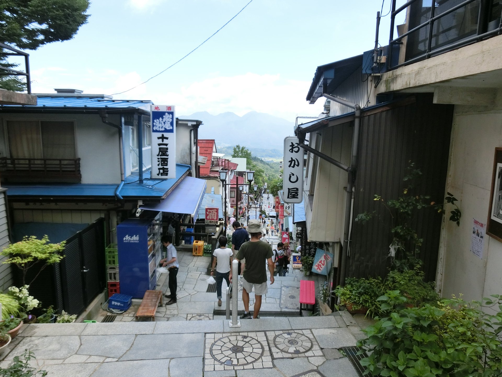 伊香保温泉の石段街を上から見下ろした眺め。両側に酒店や菓子店の看板が並び、石段の先に山並みが見える
