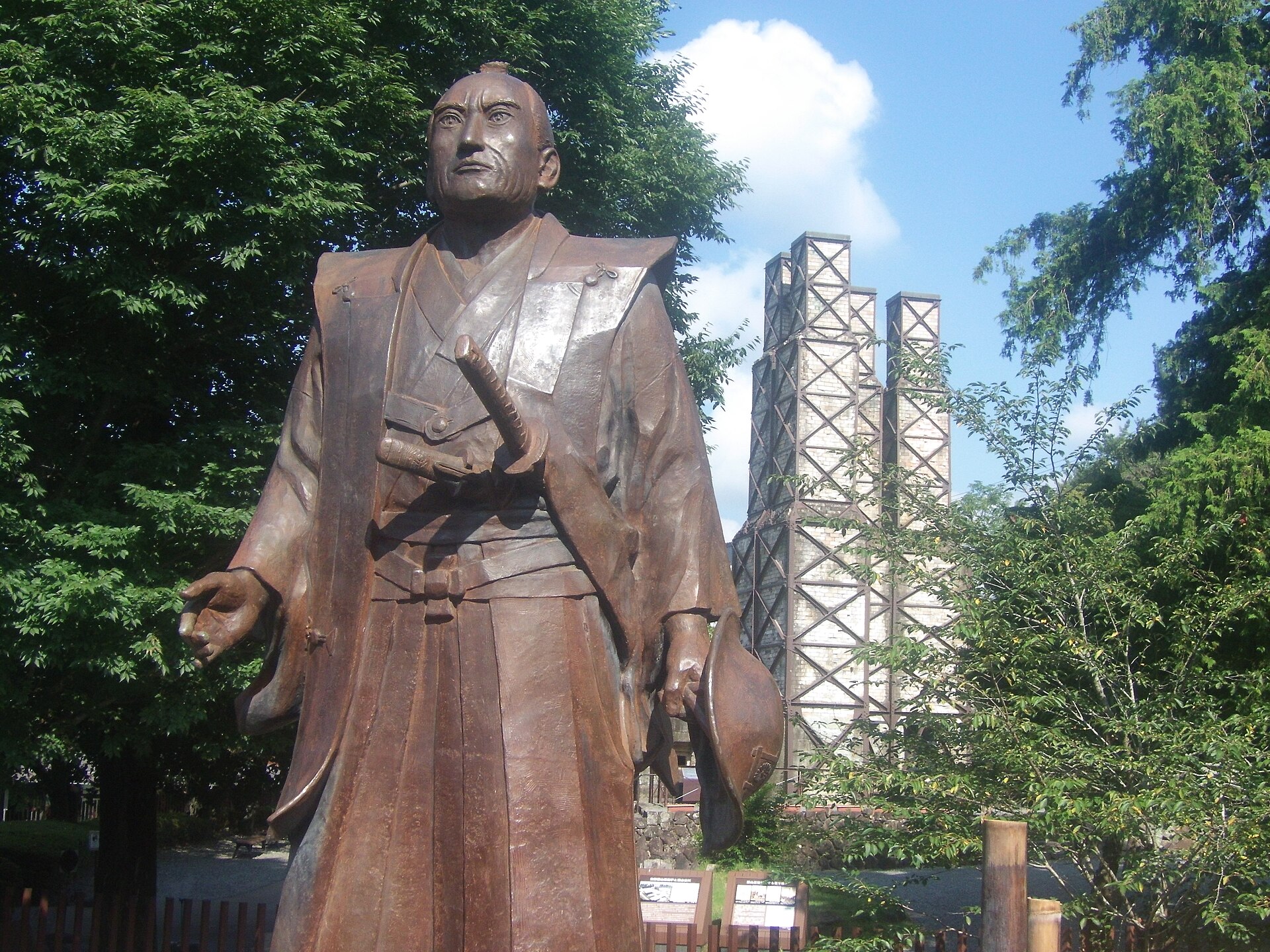手前に袴姿の江川英龍の銅像が立ち、背後に韮山反射炉の煙突が見える