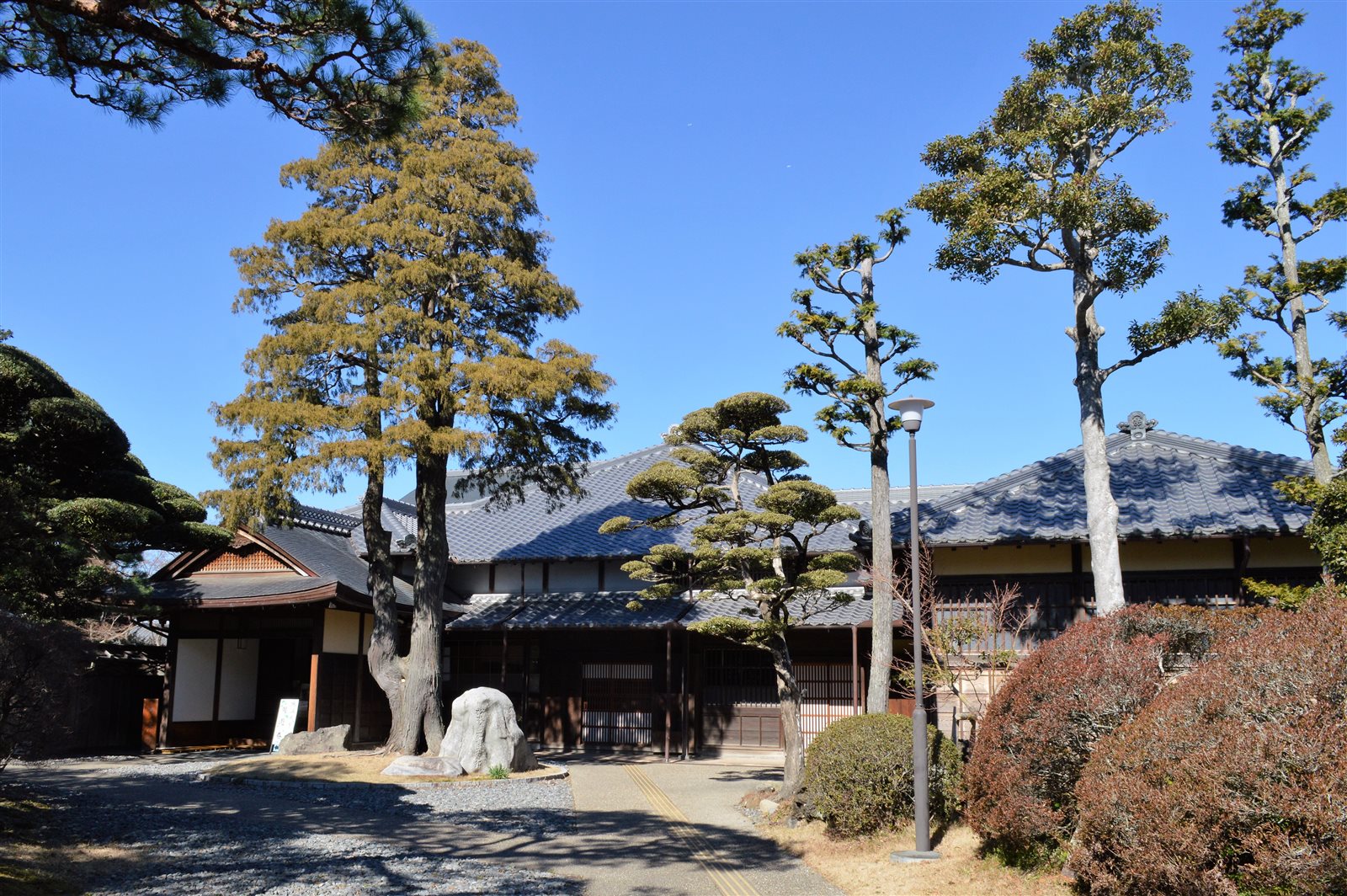 手前に松と庭木が並び、奥に瓦屋根の大きな和風の屋敷が建つ竹の丸