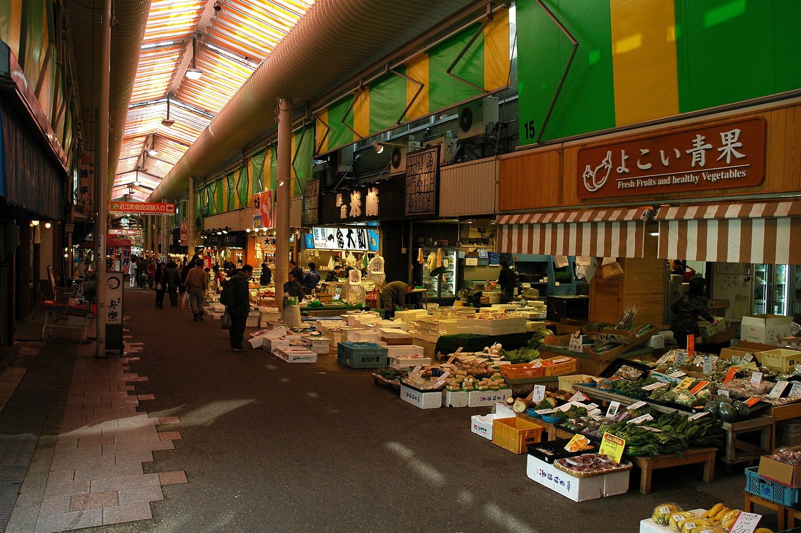 屋根のあるアーケードの下に、野菜や魚の店が並ぶ近江町市場