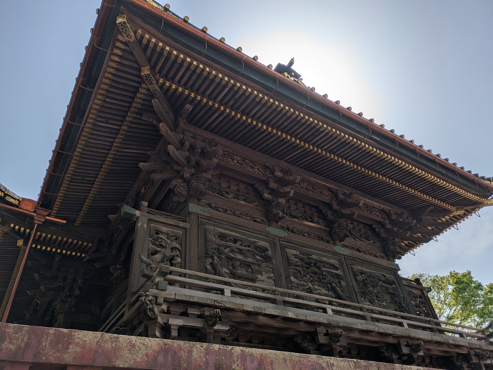 笠間稲荷神社の本殿を下から見上げた写真。深い軒の下に、壁一面を埋める木彫りの彫刻が並び、屋根の軒先に金色の飾りが見える