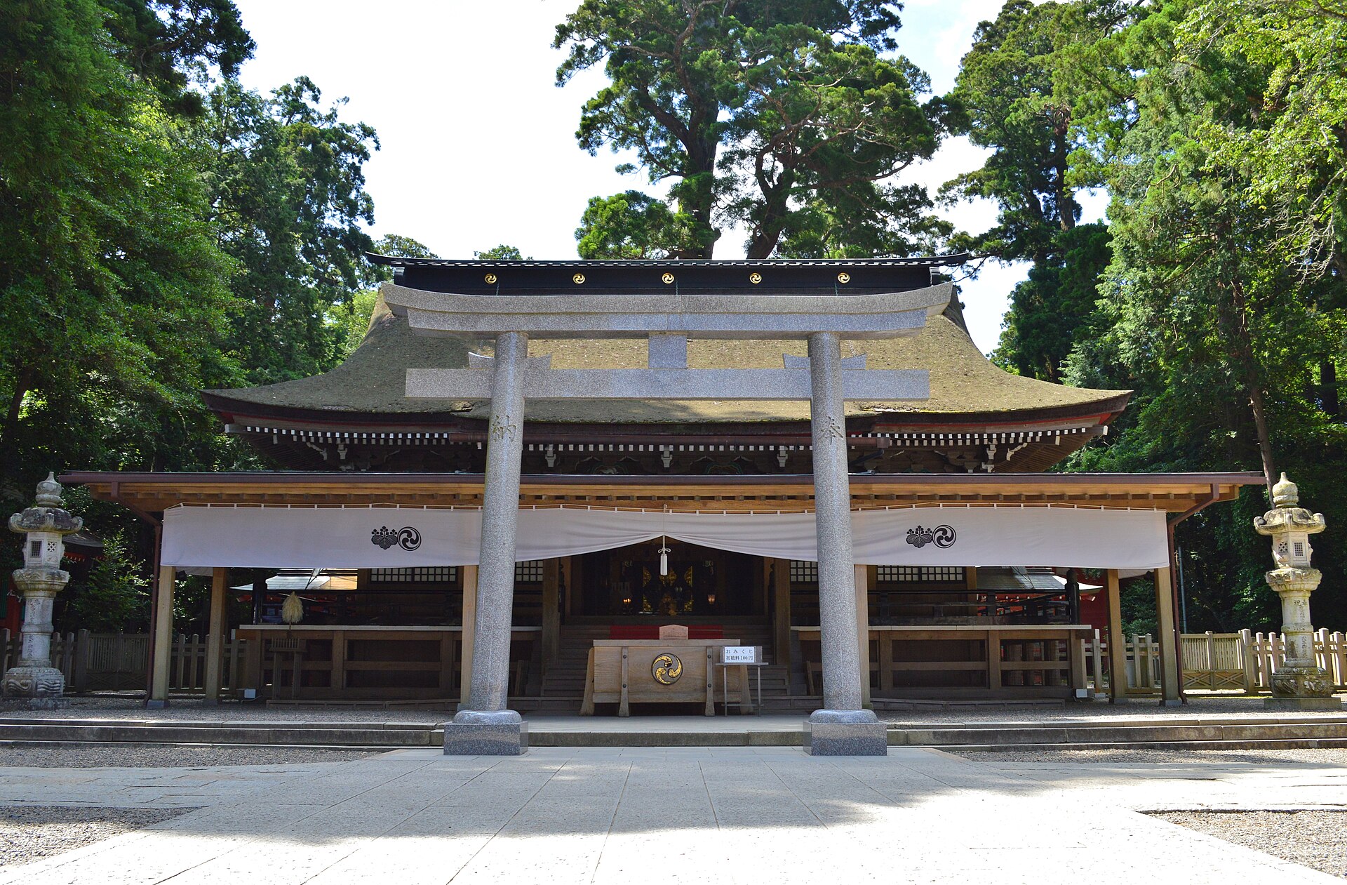 石の鳥居の向こうに、杉の木立に囲まれた鹿島神宮の拝殿が見える