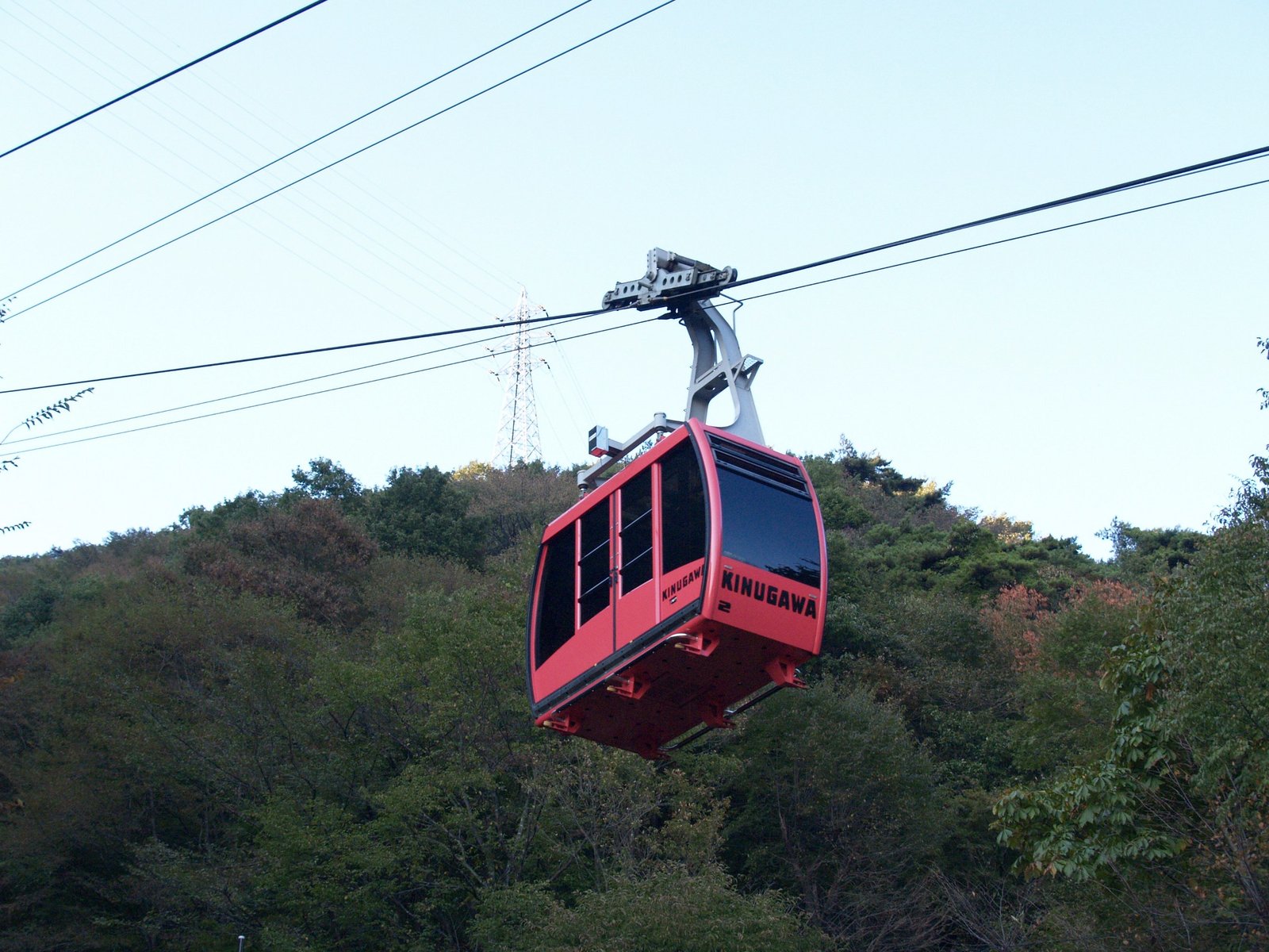 緑の山を背に、赤い車体のロープウェイのゴンドラが空中を進む