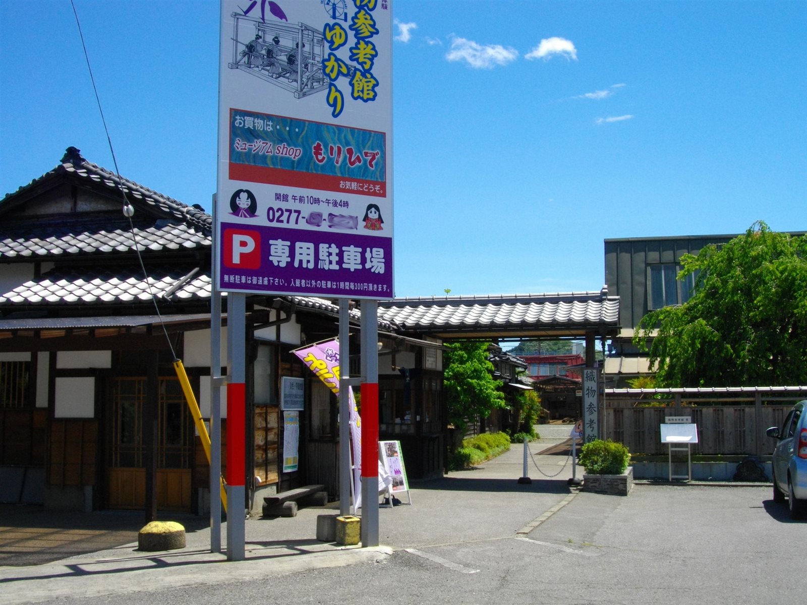 瓦屋根の入口の前に、織物参考館の看板と専用駐車場の看板が立つ