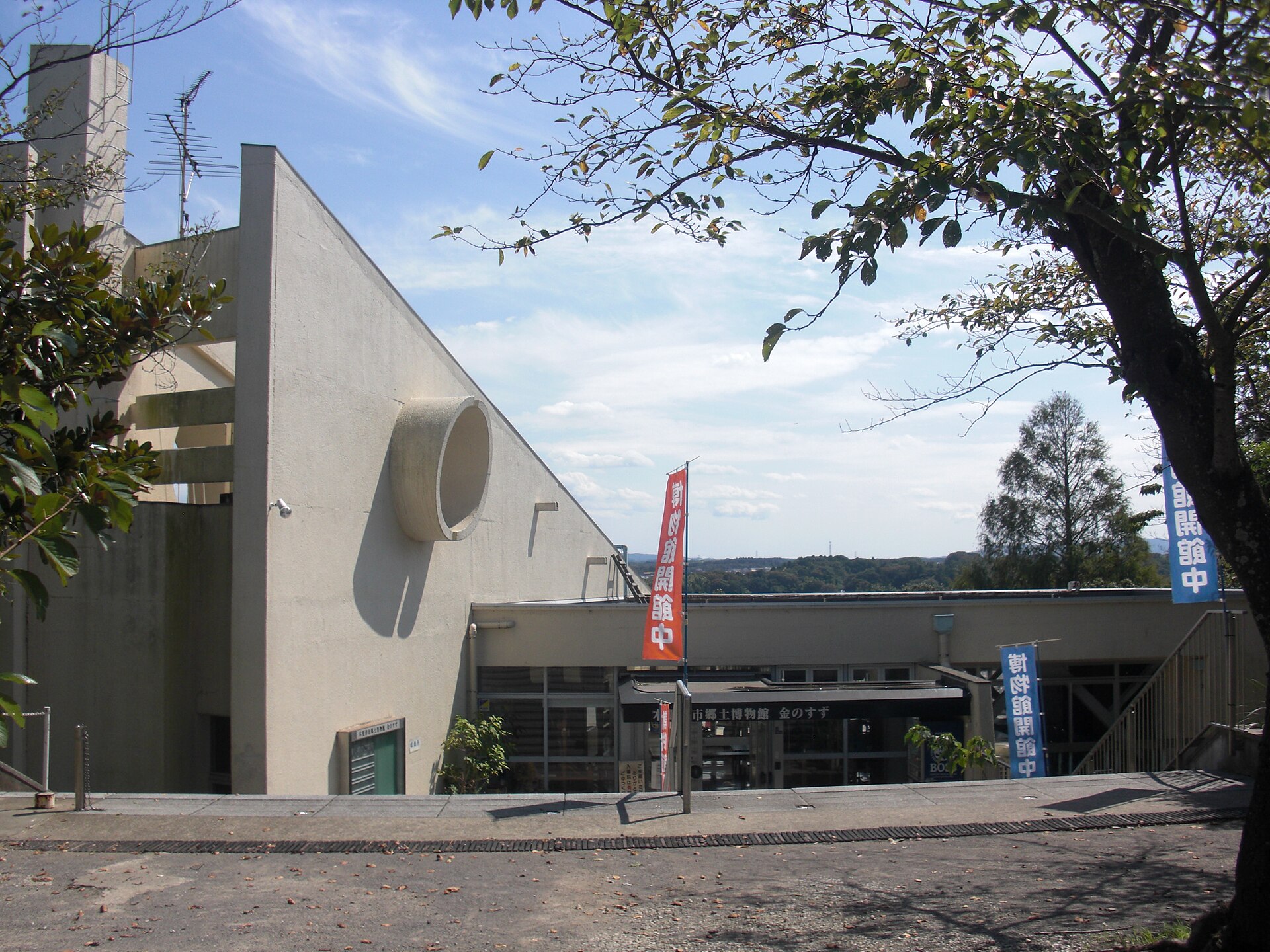 白い壁に丸い穴のあいた郷土博物館金のすずの建物と、のぼりの立つ入口
