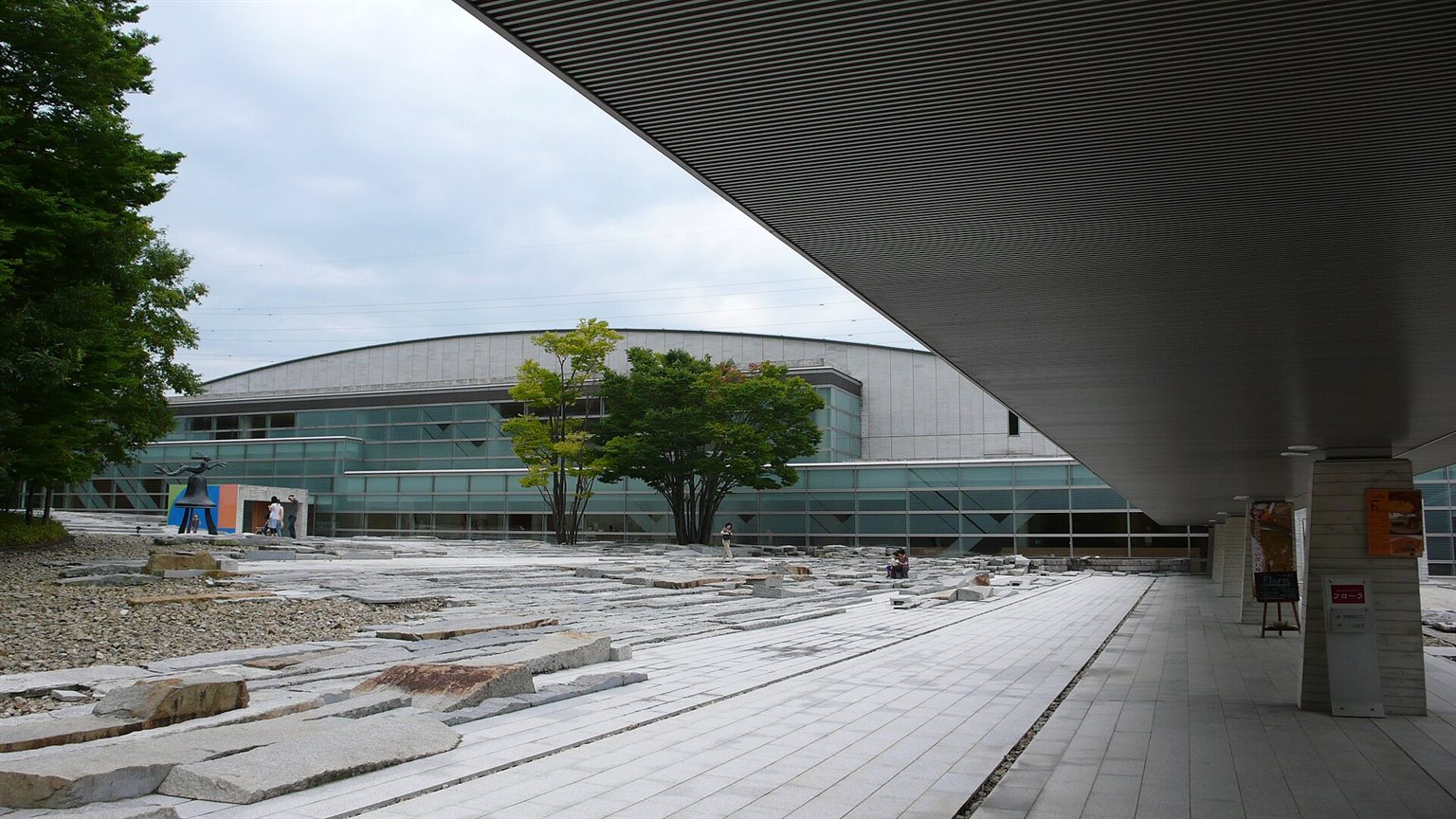 石を敷いた広場の向こうに、ガラス張りの壁と曲線の屋根をもつ美術館の建物