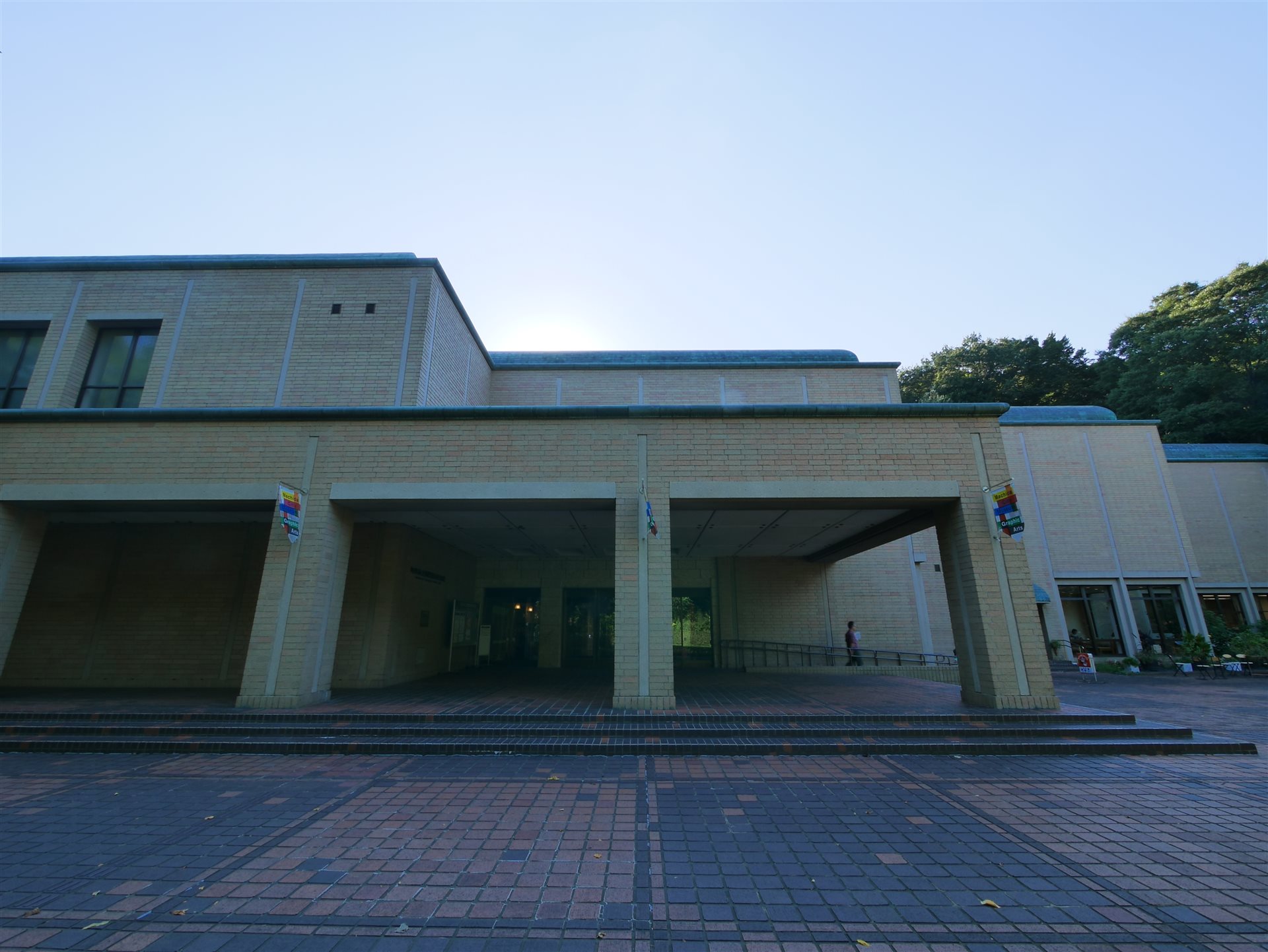 レンガ色の壁の庇の下に入口が並ぶ、町田市立国際版画美術館の外観