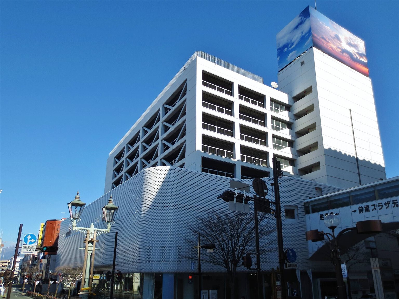 銀色の穴あきパネルで覆われた壁面と、空の写真の看板をもつ、アーツ前橋の建物