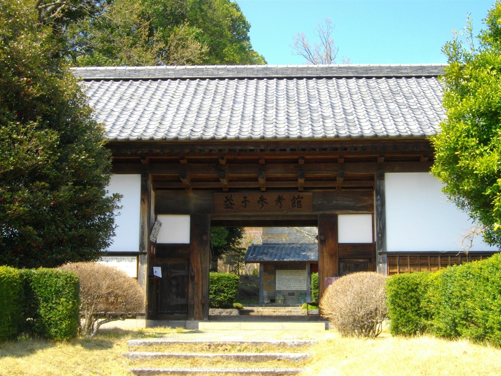 低い石段の先に建つ瓦屋根の長屋門と、門の奥に見える建物。濱田庄司記念益子参考館の入口