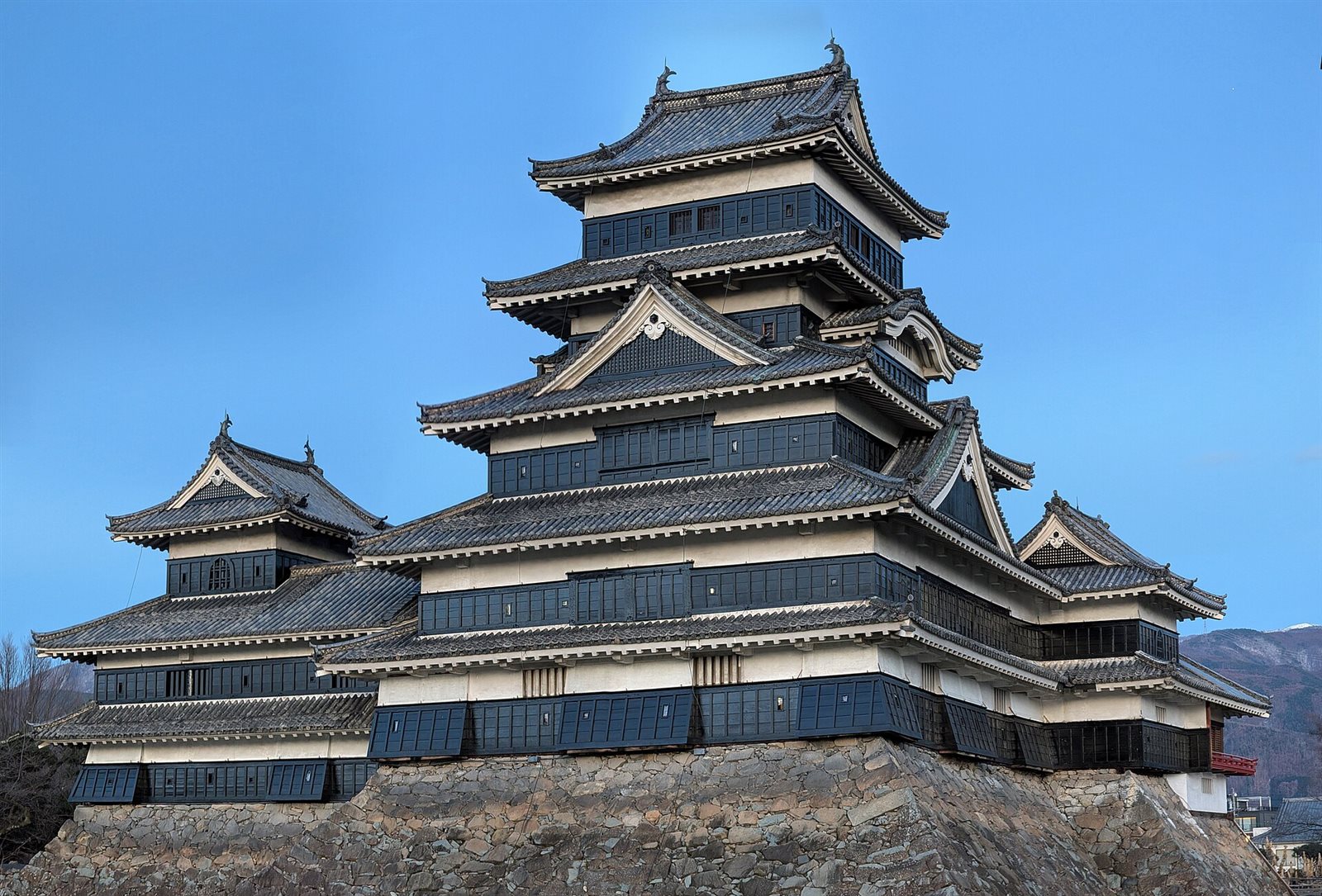 青い空を背に、石垣の上に重なる屋根がそびえる松本城の天守