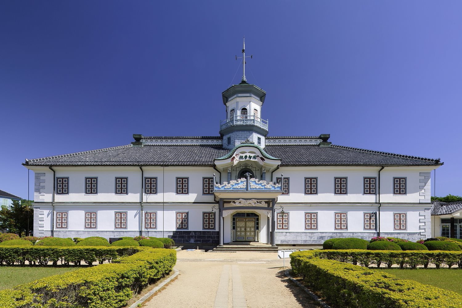 中央に塔屋をのせた、白い壁の2階建ての旧開智学校の校舎正面
