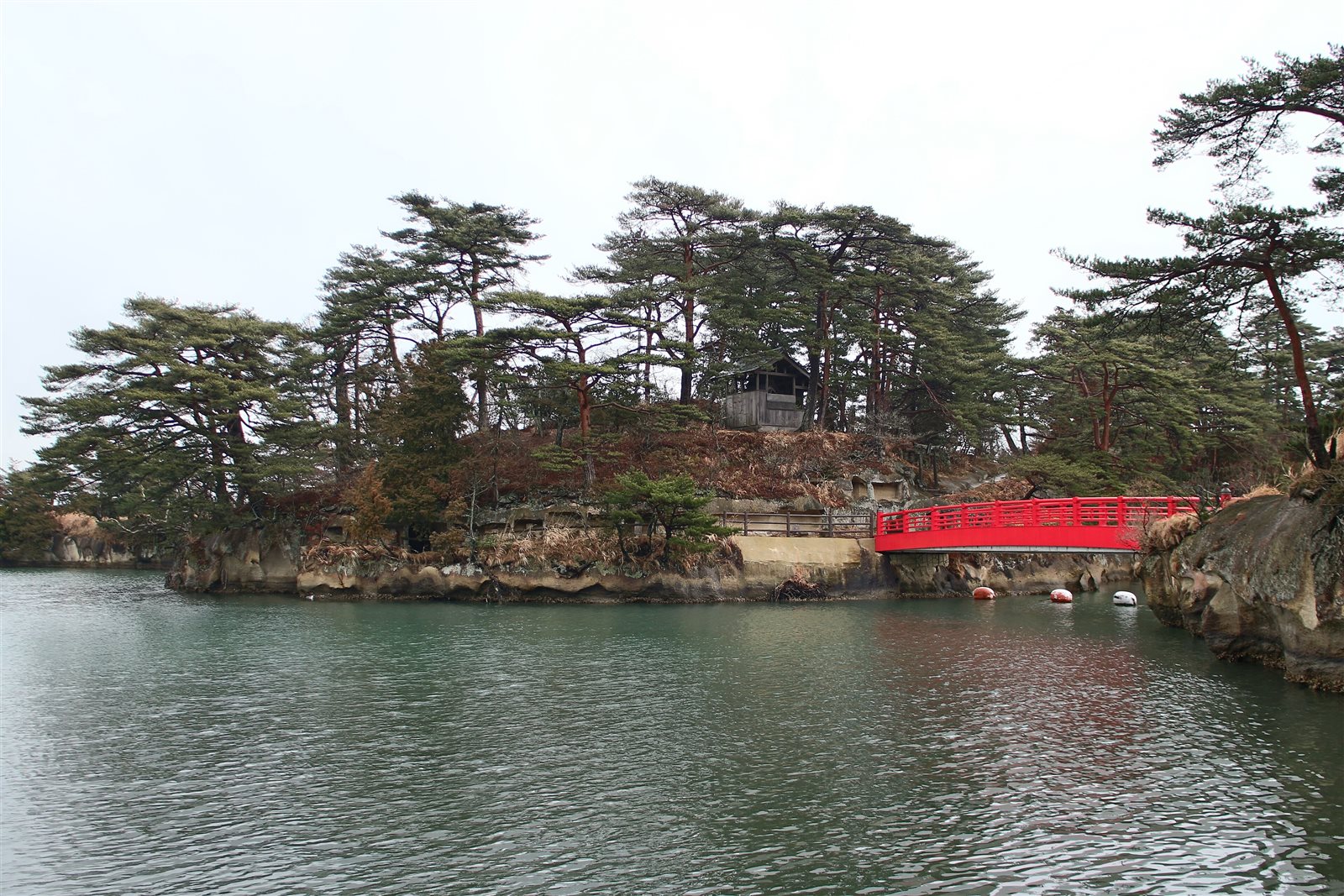 松の木が茂る雄島と、島へ渡る朱塗りの渡月橋。手前は緑色の海