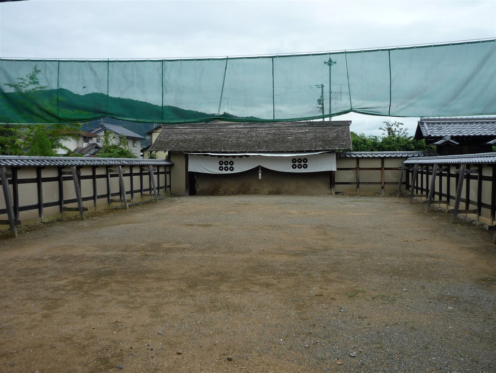 土の広場の向こうに、六つの丸い紋の白い幕が掛かる土の的場と、白壁の塀が並ぶ弓術所