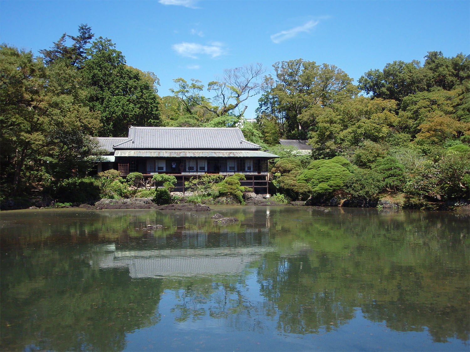 楽寿園の小浜池ごしに見た楽寿館。水際に黒い溶岩が並ぶ