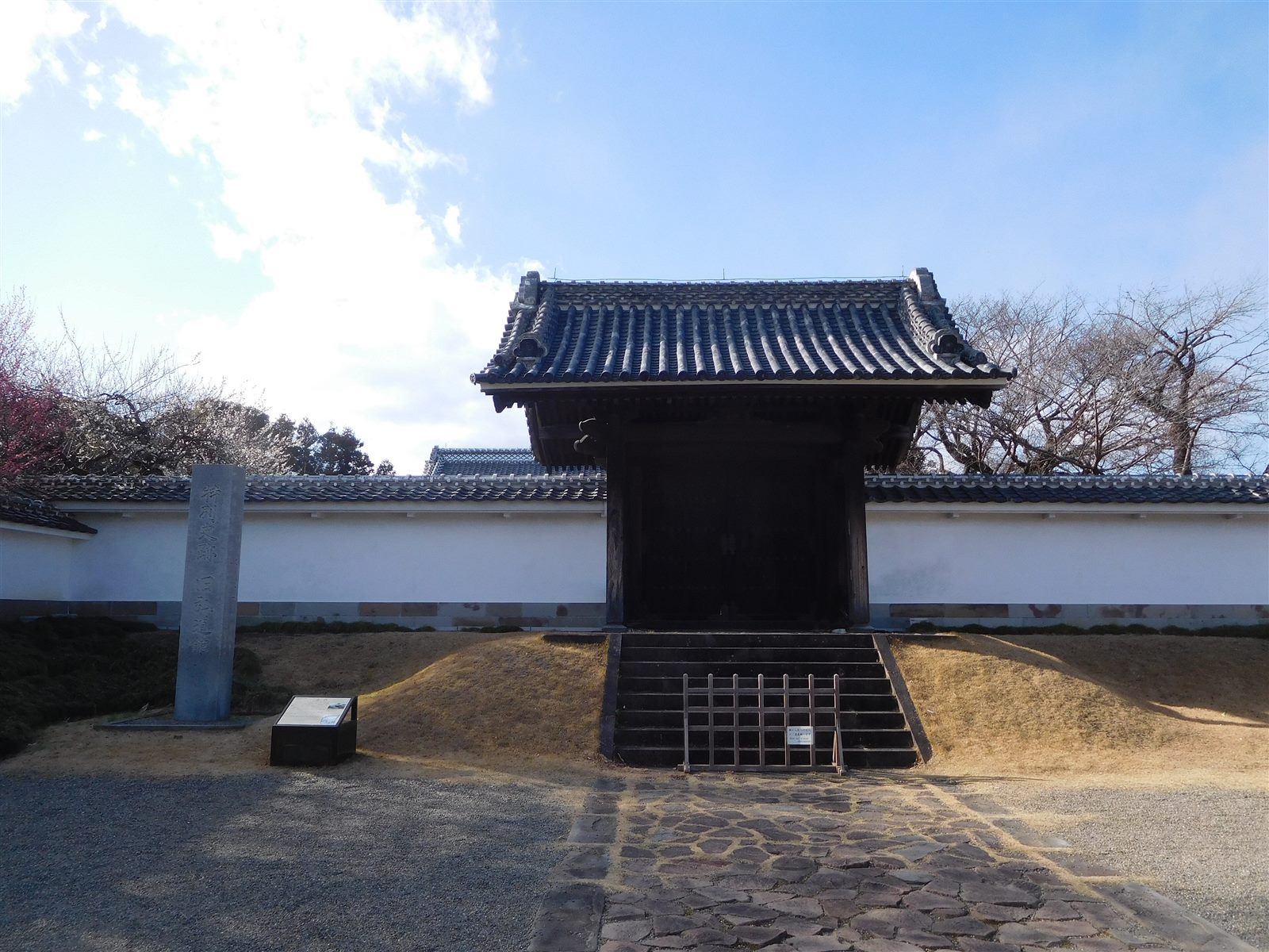 石畳の先に、瓦屋根の門が白い塀の中に建つ