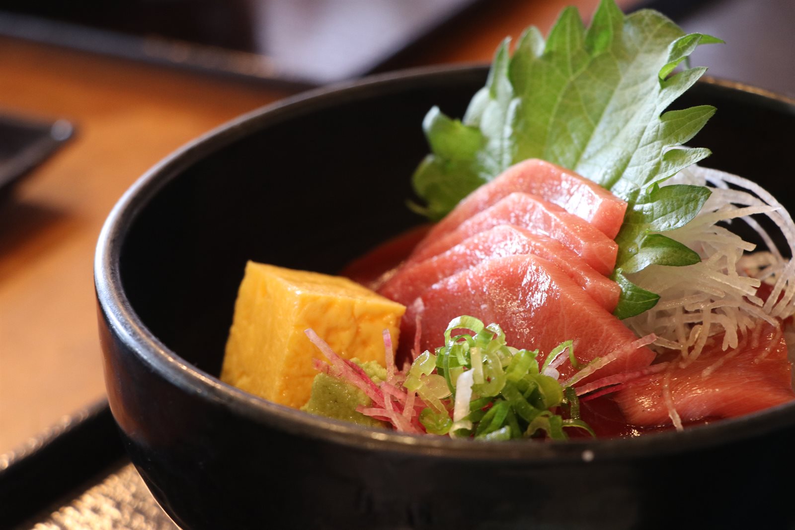黒い丼に盛られたまぐろの漬け丼。上に中トロの切り身、下に漬けのまぐろが載り、大葉・大根のつま・刻みねぎ・玉子焼きが添えられている