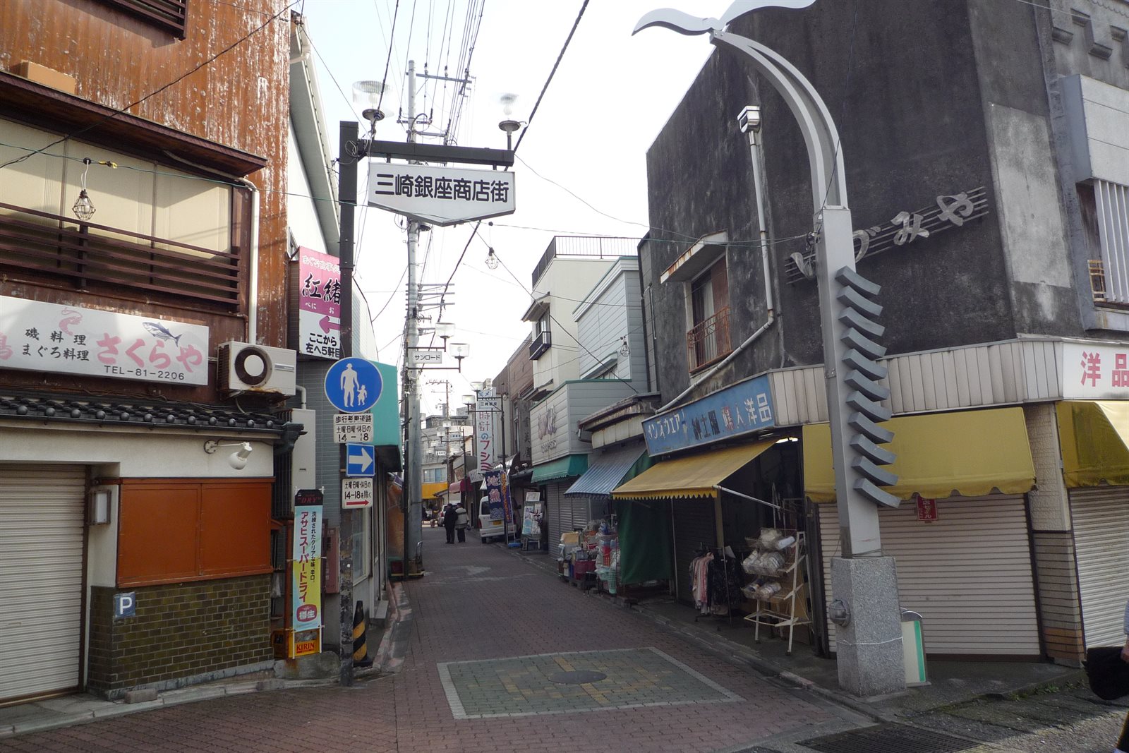 三崎の商店街。「三崎銀座商店街」と書かれた看板が通りの上に掛かり、両側に商店や、まぐろ料理と書かれた看板を出した店が並んでいる