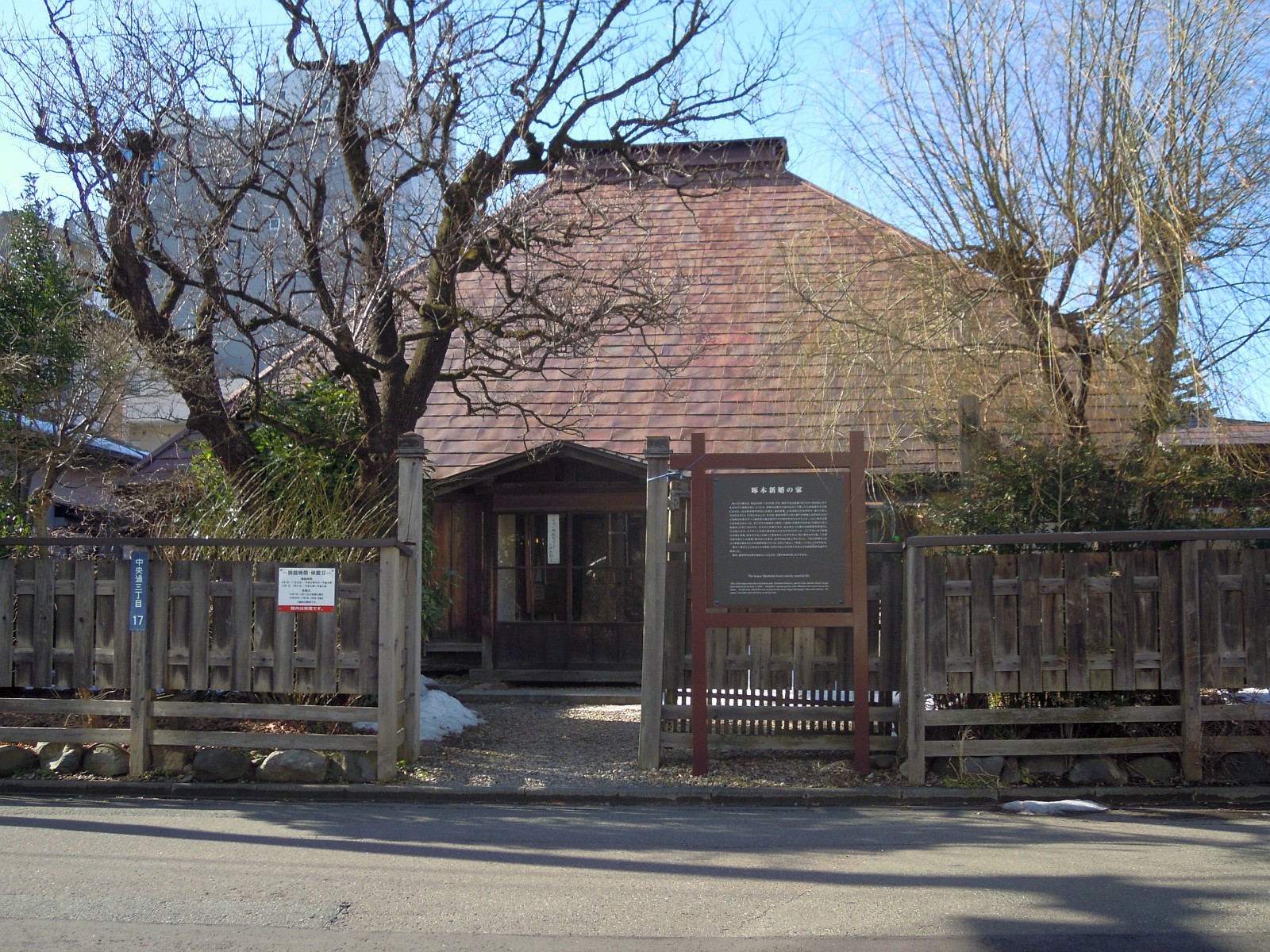 門の奥に、赤茶色の屋根の大きな平屋が建つ、啄木新婚の家