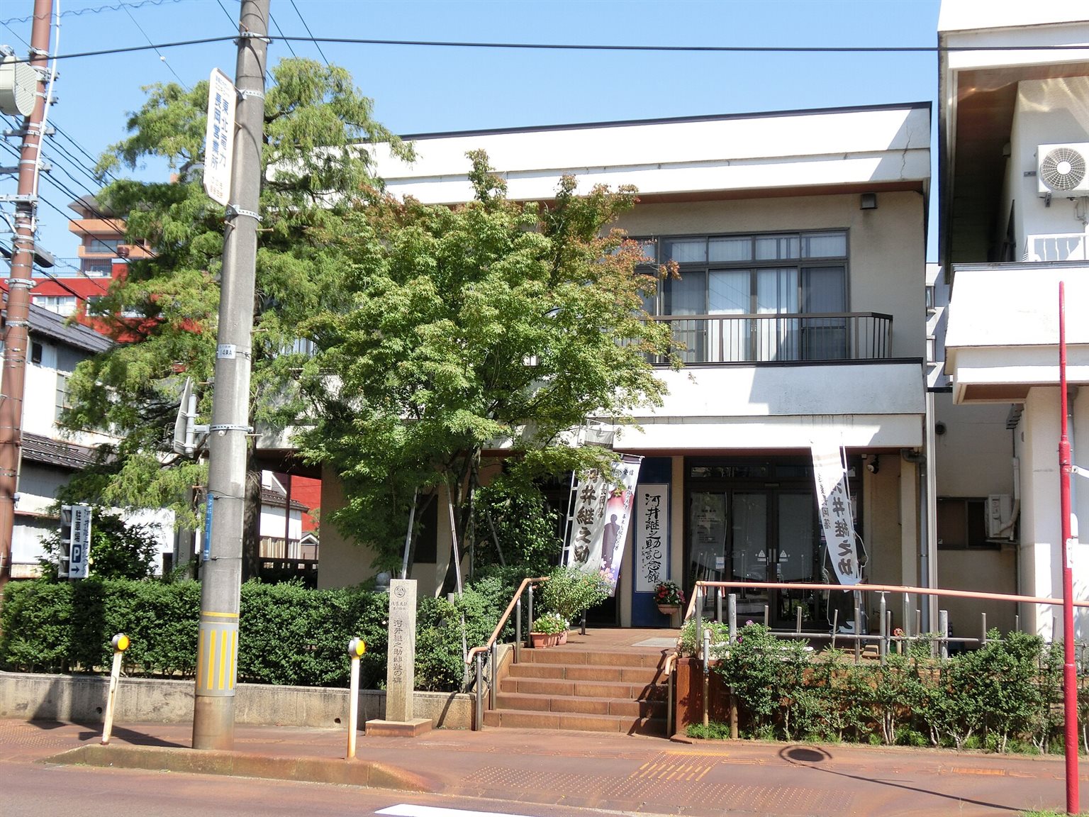 木々の奥に建つ、二階建ての河井継之助記念館の正面と、石段の脇に立つ石碑