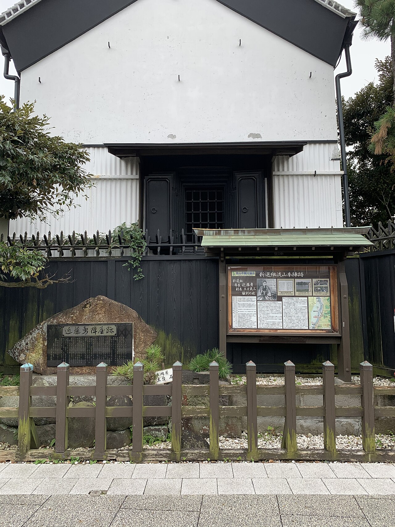 白い土蔵の前に立つ、近藤勇陣屋跡の石碑と案内板