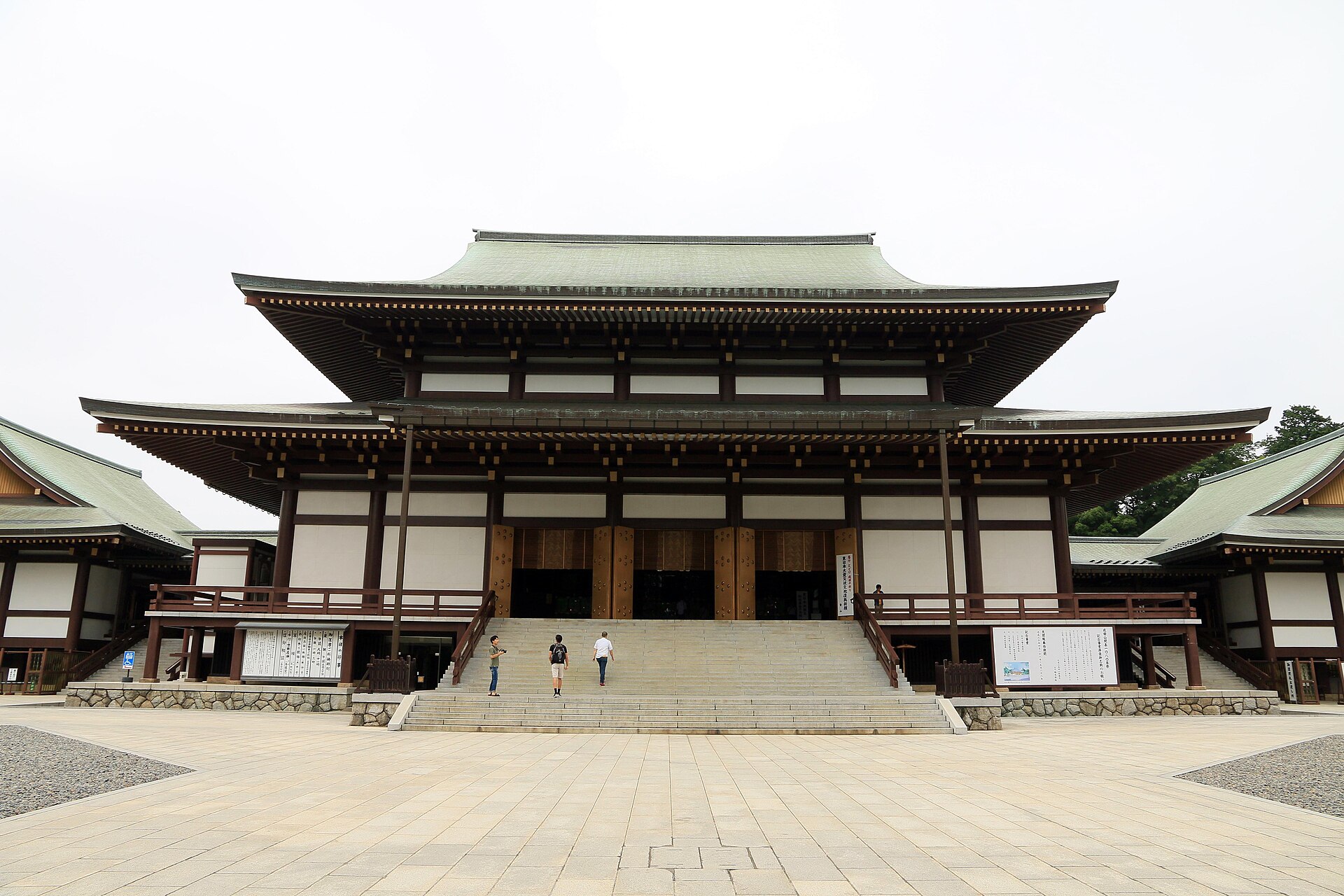 成田山新勝寺の大本堂。二重の屋根を持つ木造の大きな堂が正面に建ち、手前に石畳の広場と堂へ上がる階段がある
