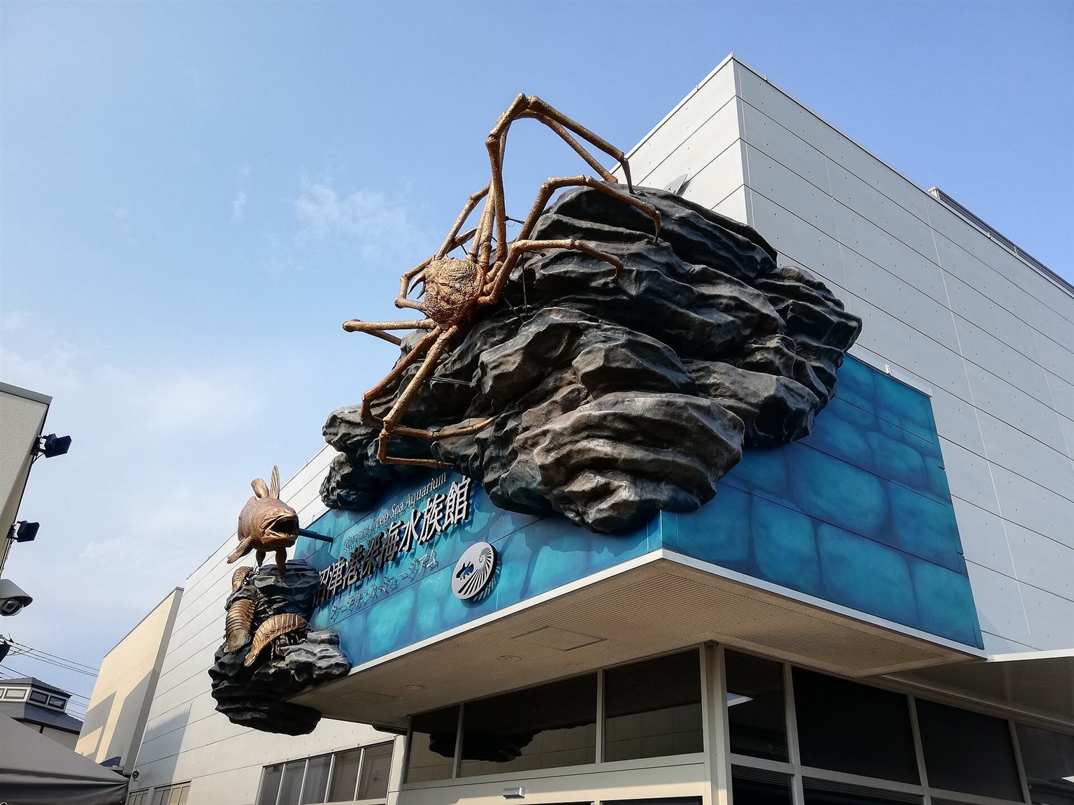 大きなタカアシガニの像が岩の上に載る、沼津港深海水族館の入口の外観
