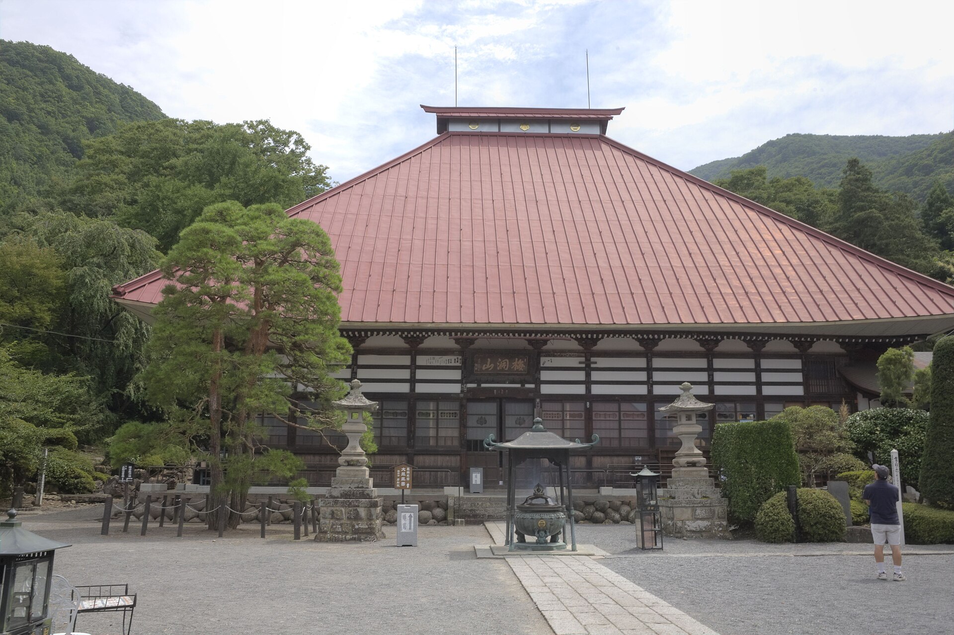 赤い屋根の大きな本堂と、石灯籠、香炉のある岩松院の境内