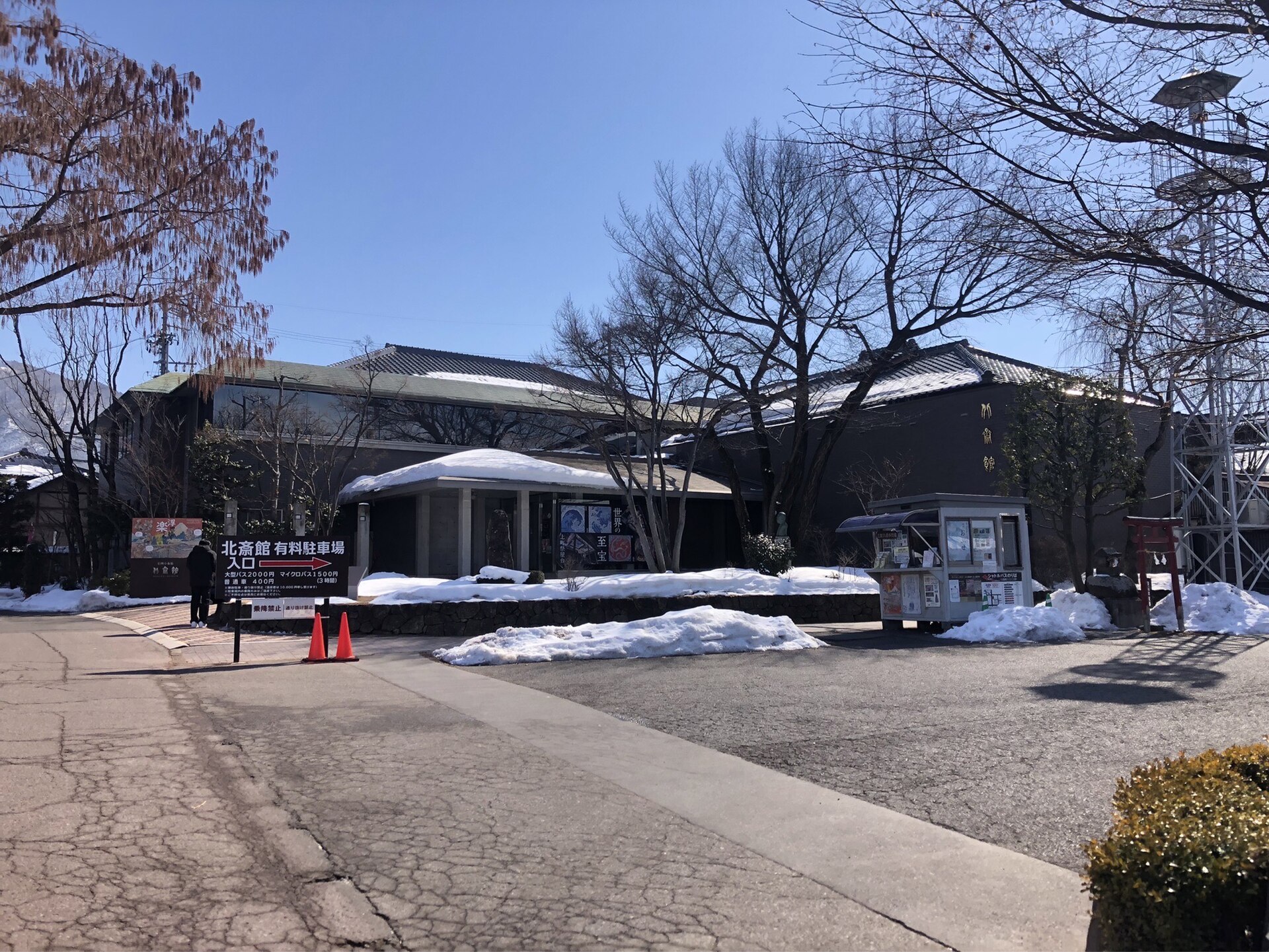 雪の残る道の先に建つ、北斎館の入口と展示の案内看板