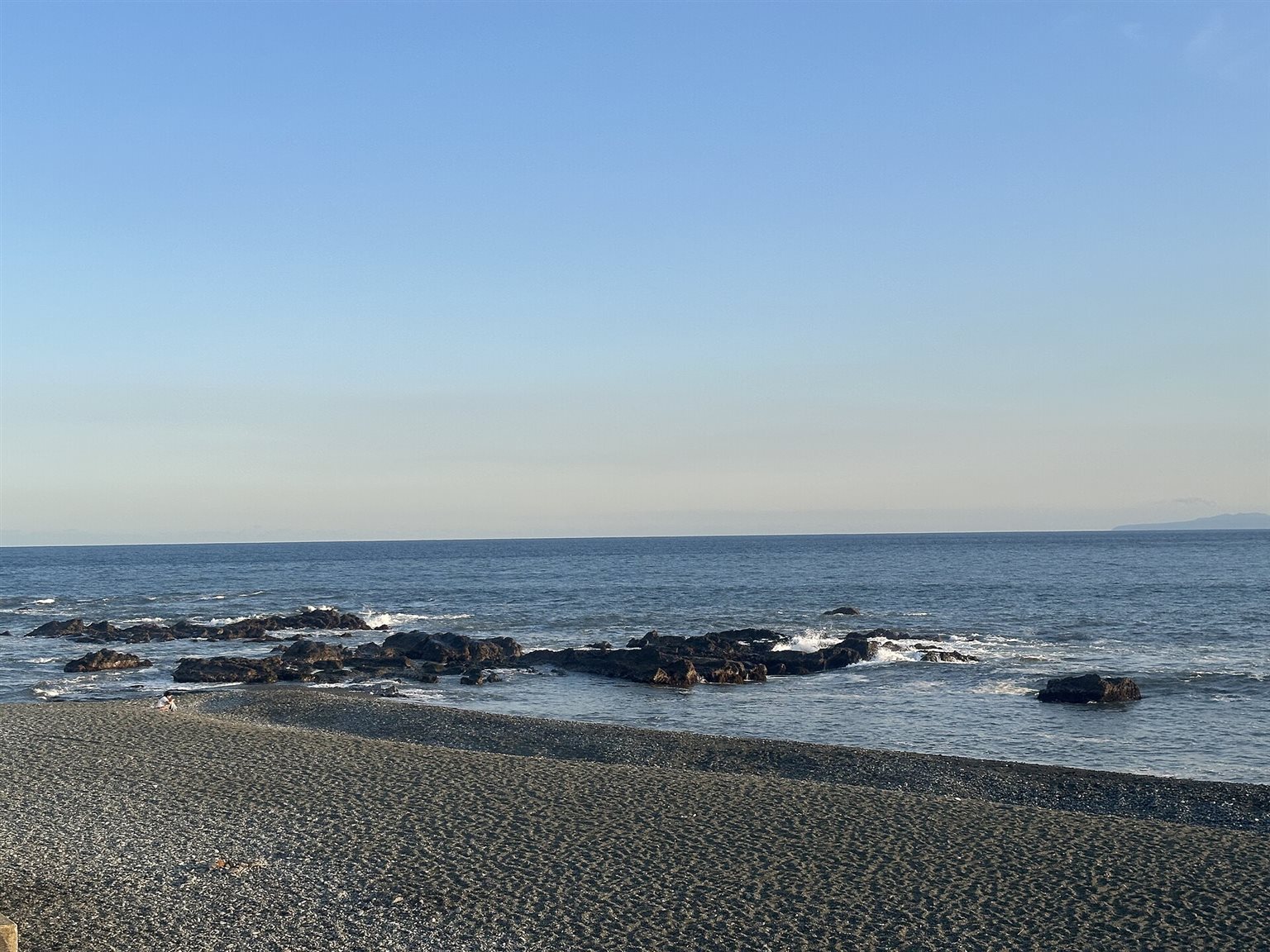 砂利の浜の先に岩場が続き、その向こうに相模湾が広がる照ヶ崎海岸