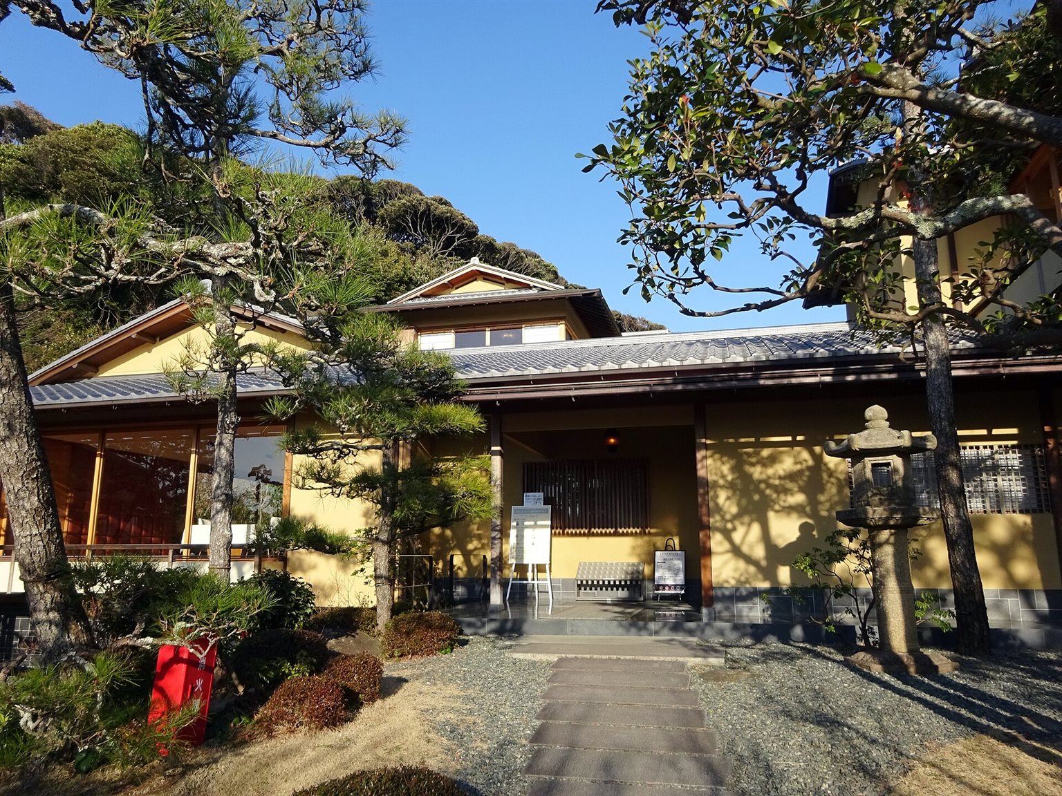 松と庭木に囲まれた、黄色い壁の平屋建ての旧吉田茂邸の母屋と、石灯籠