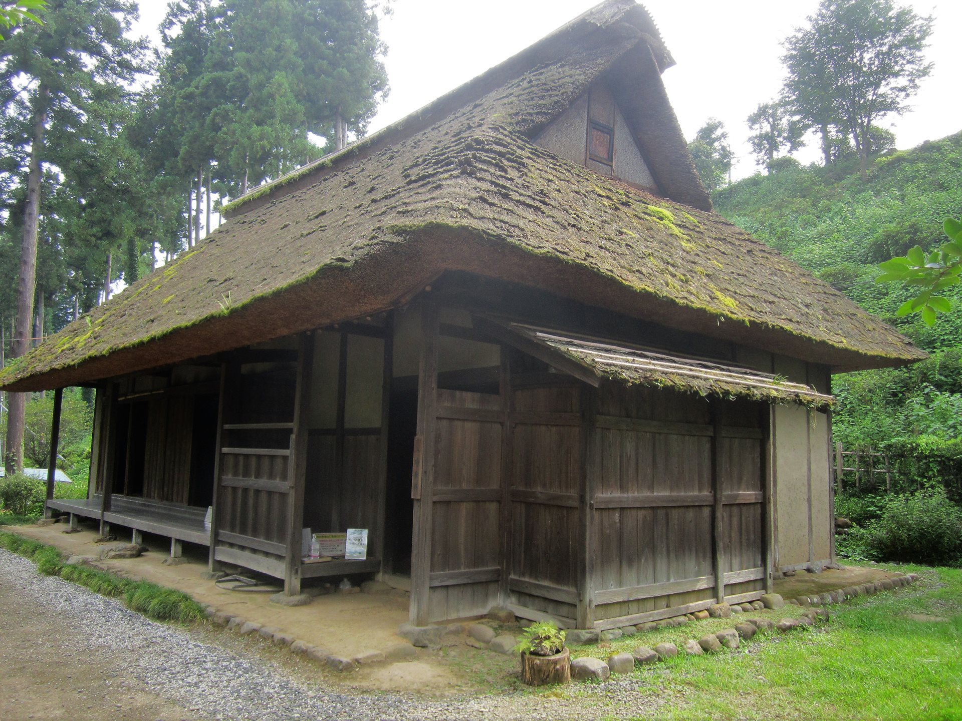 釜の淵公園に建つ旧宮崎家住宅。苔の生えた茅葺き屋根が深く張り出し、正面に板戸と縁側が並んでいる