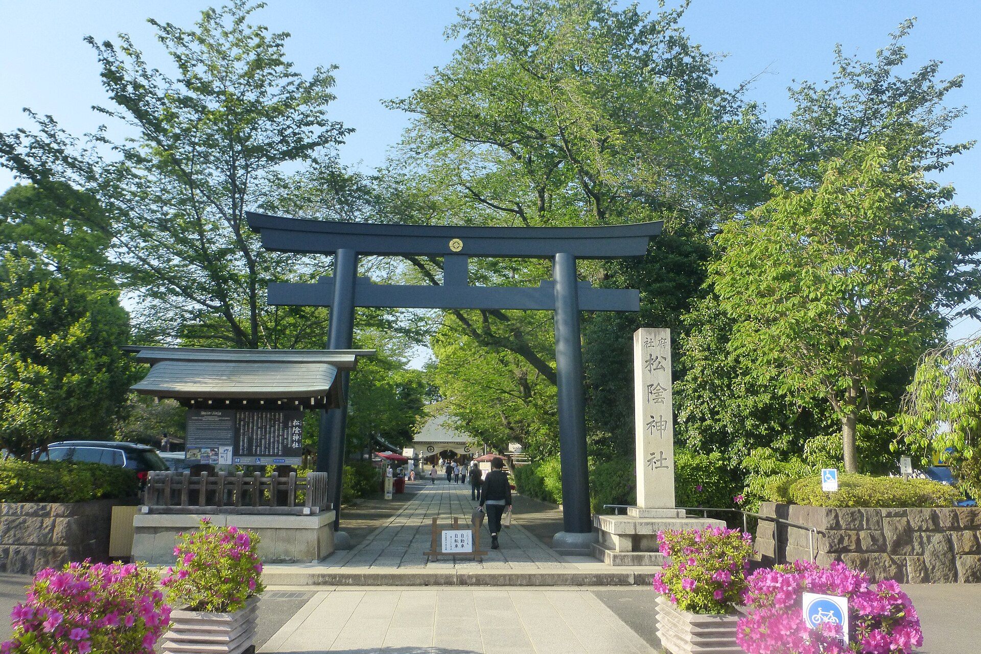 緑の木々に囲まれた参道の先に立つ、松陰神社の黒い鳥居と社号標