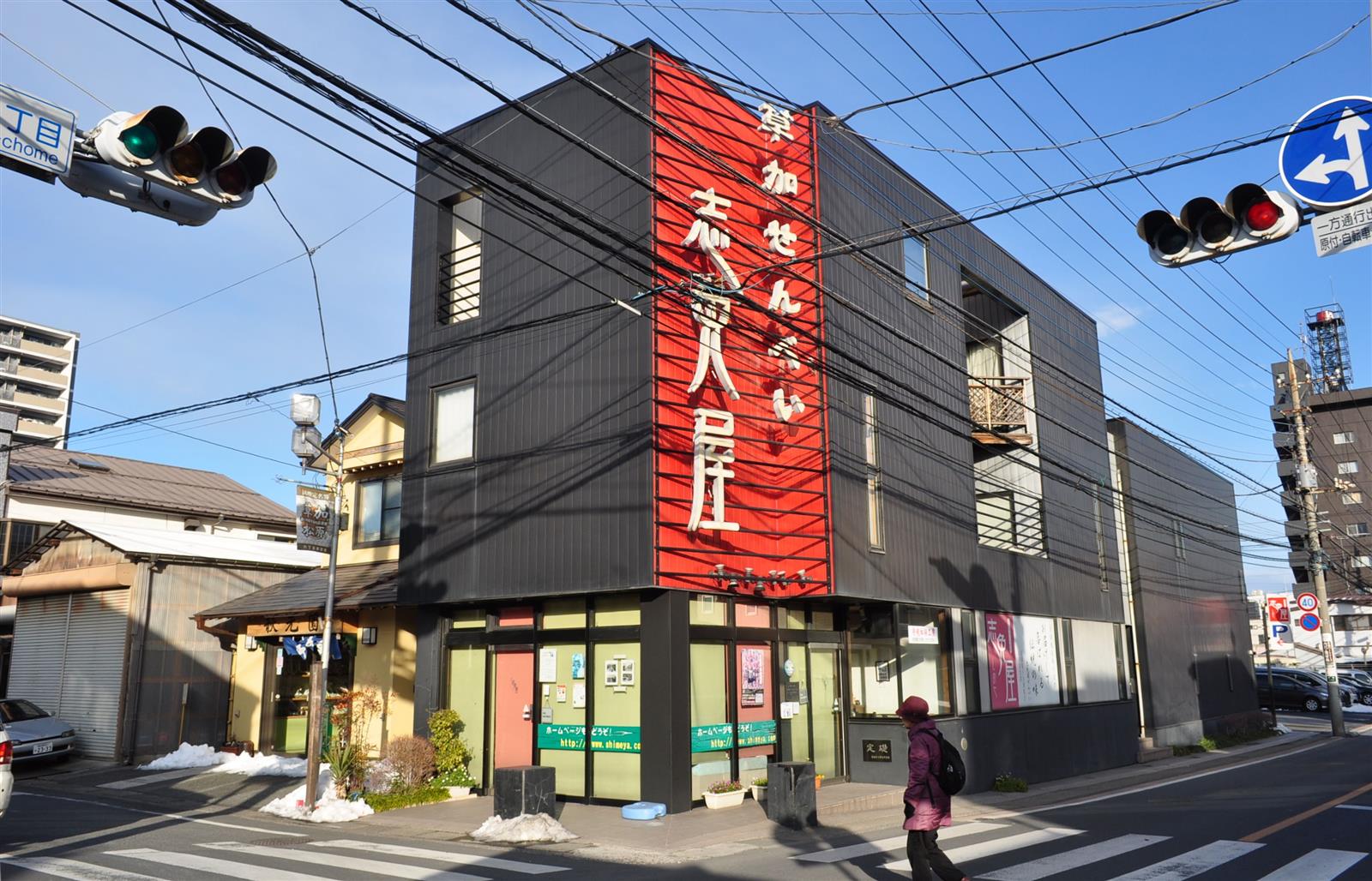 赤い看板に「草加せんべい 志免屋」と書かれた、交差点の角に建つ黒い建物