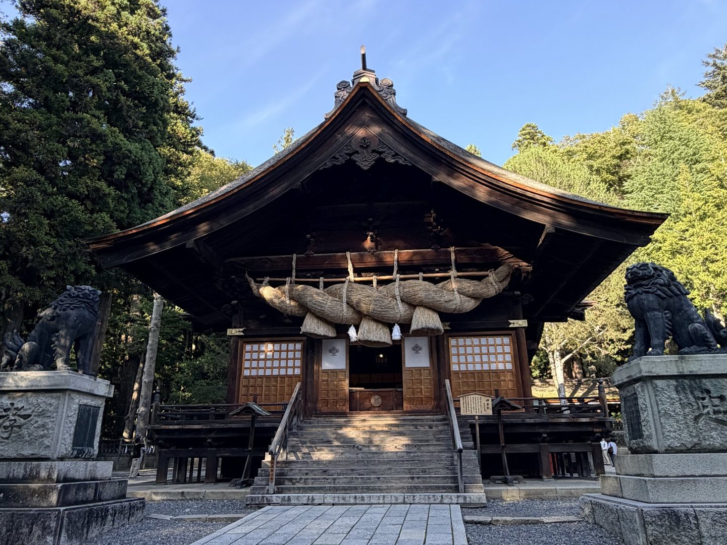 大きな注連縄のかかる神楽殿と、石の台座の上に座る左右の青銅の狛犬