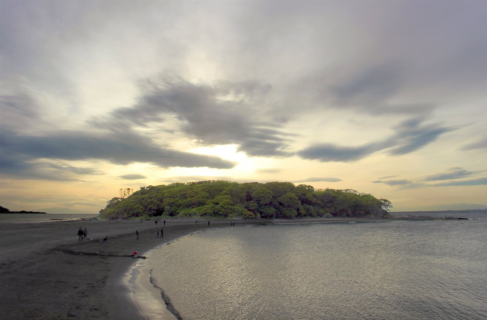 夕暮れの雲の下、砂浜の先に木々で覆われた沖ノ島が横たわる