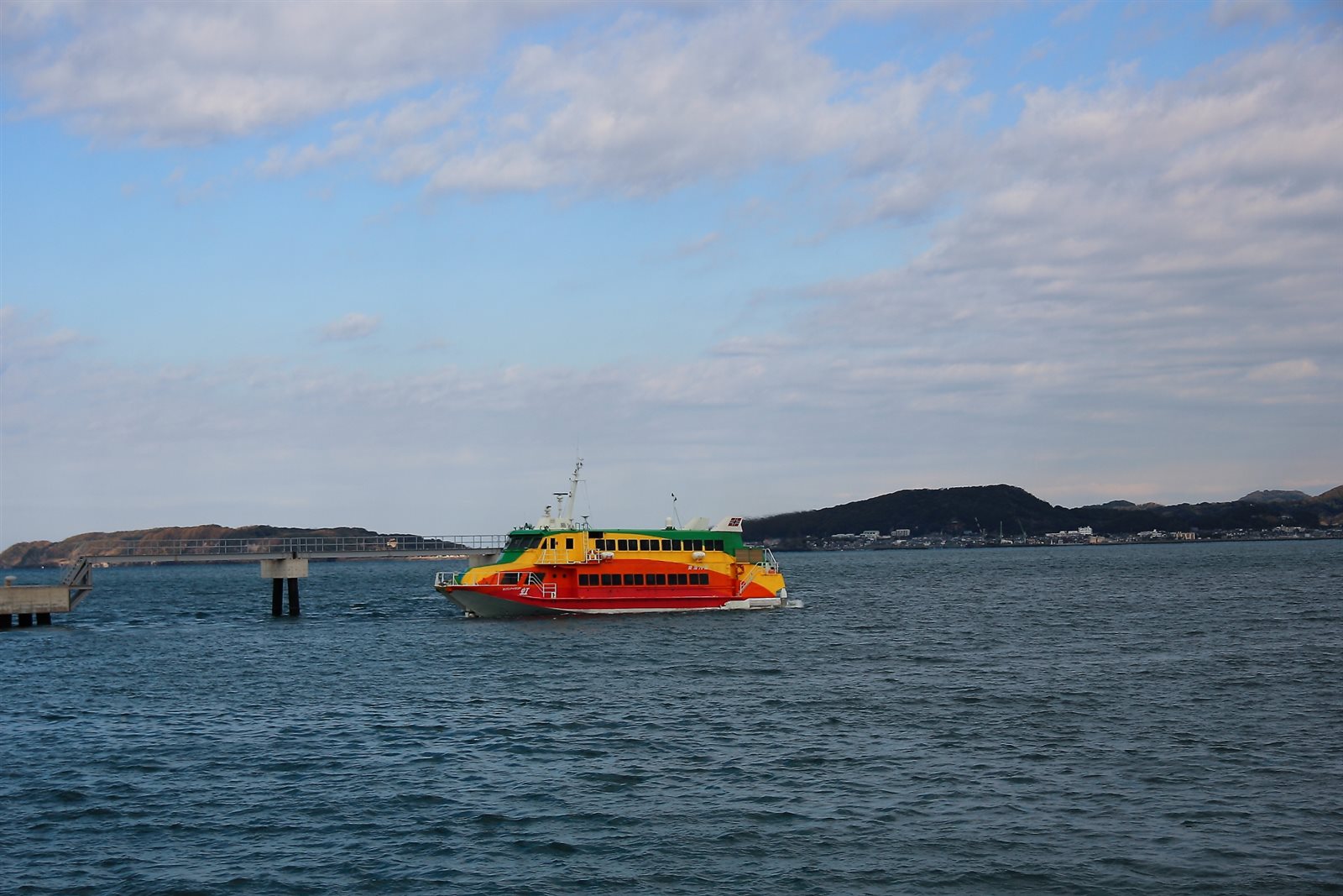穏やかな館山湾を進む赤と黄色の高速船と、その奥に延びる桟橋