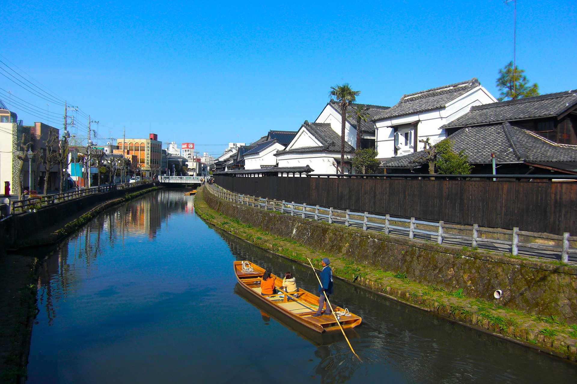 栃木市の巴波川。右岸に黒塀と白壁の土蔵が続き、川面を船頭の操る小舟が進んでいる